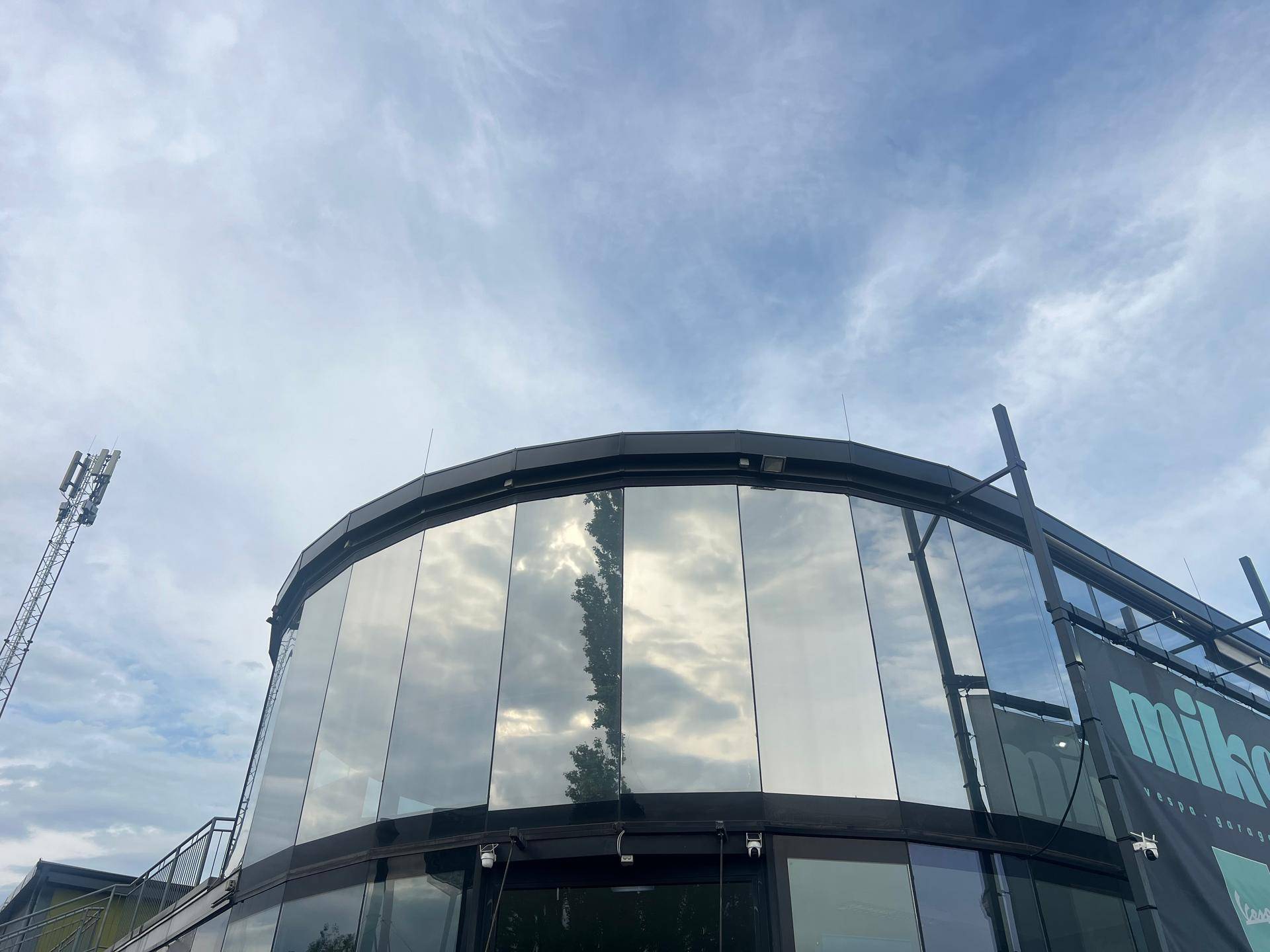 Detailansicht der reflektierenden Glasfassade des modernen Gebäudes unter einem weiten Himmel.