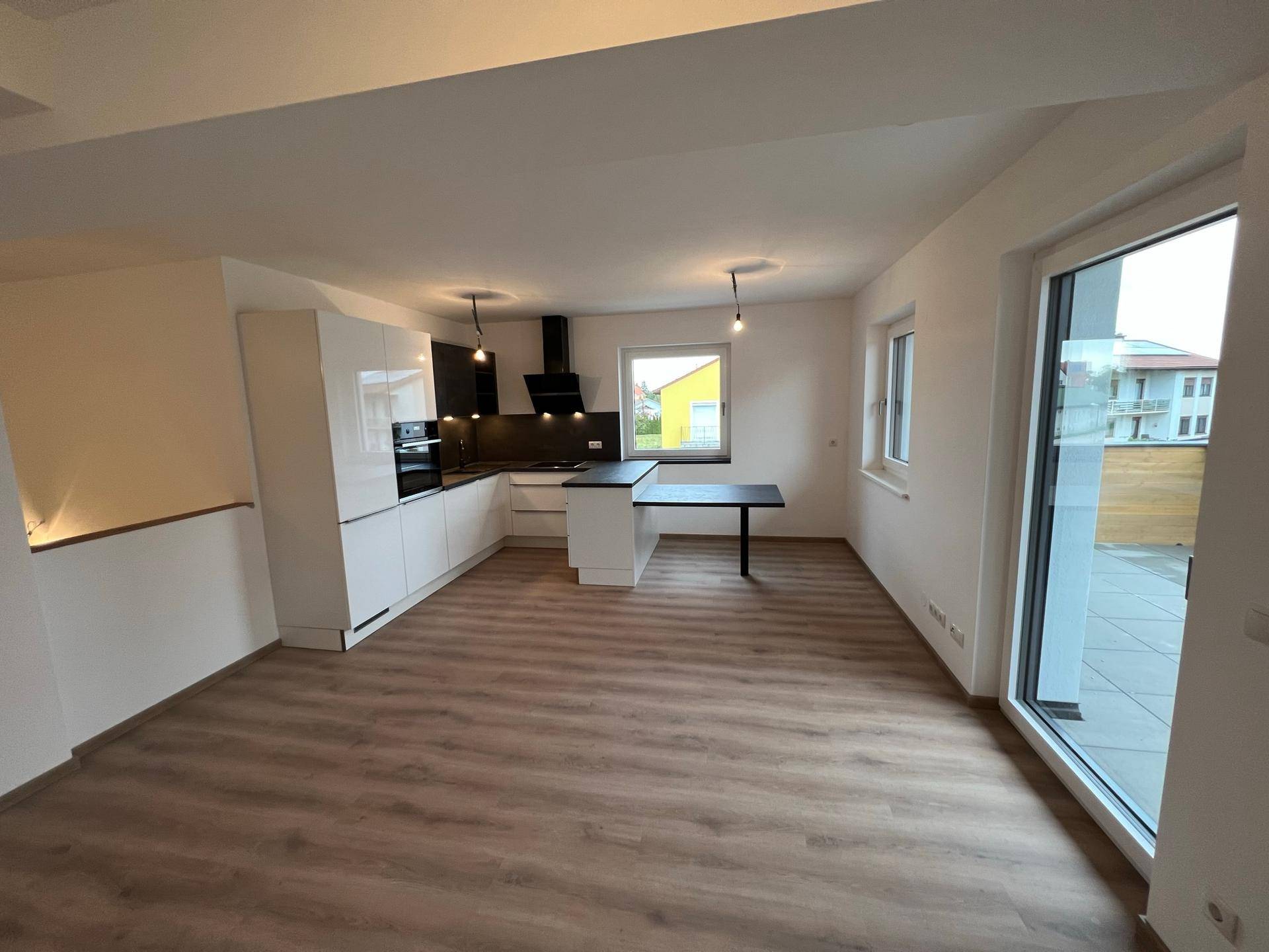 Heller, offener Wohnbereich mit integrierter Küche, Laminatboden und Zugang zu einer Terrasse.