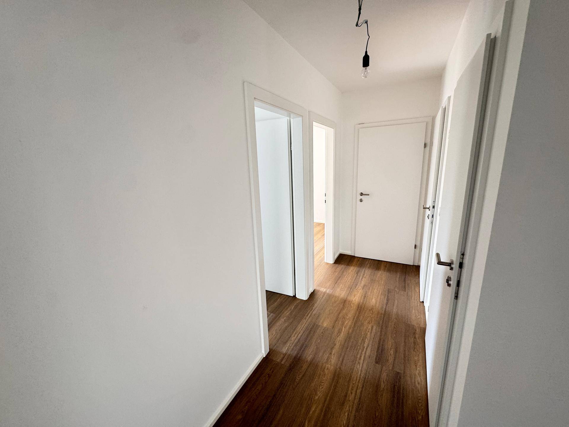 Langer, heller Flur mit Laminatboden und mehreren weißen Türen zu den Zimmern.