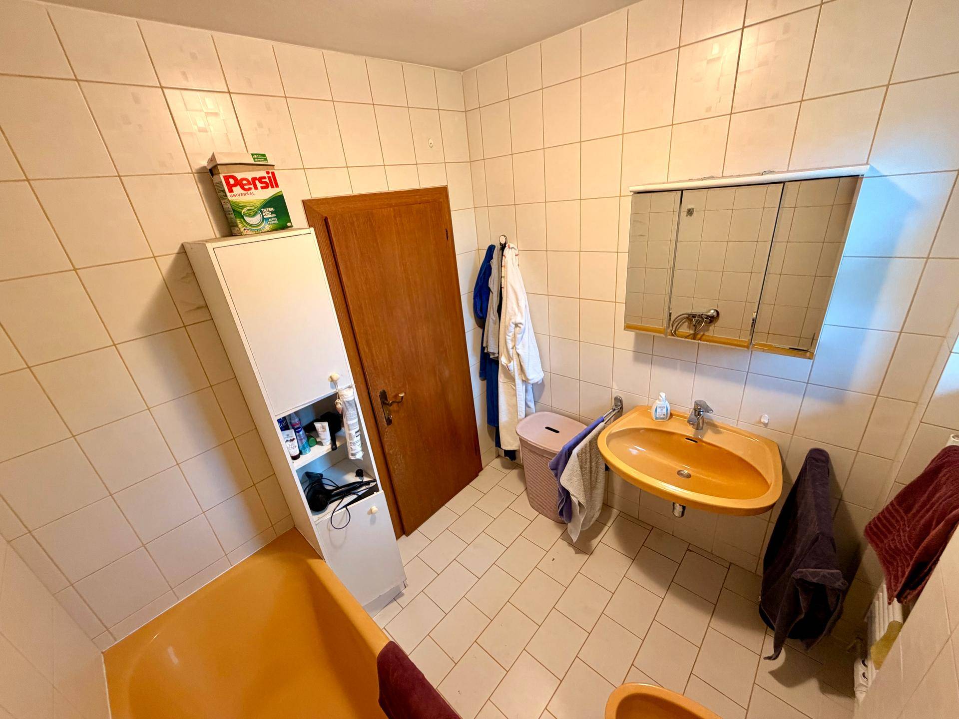 Badezimmer mit orangefarbener Badewanne und Waschbecken, gefliesten Wänden und Spiegelschrank.