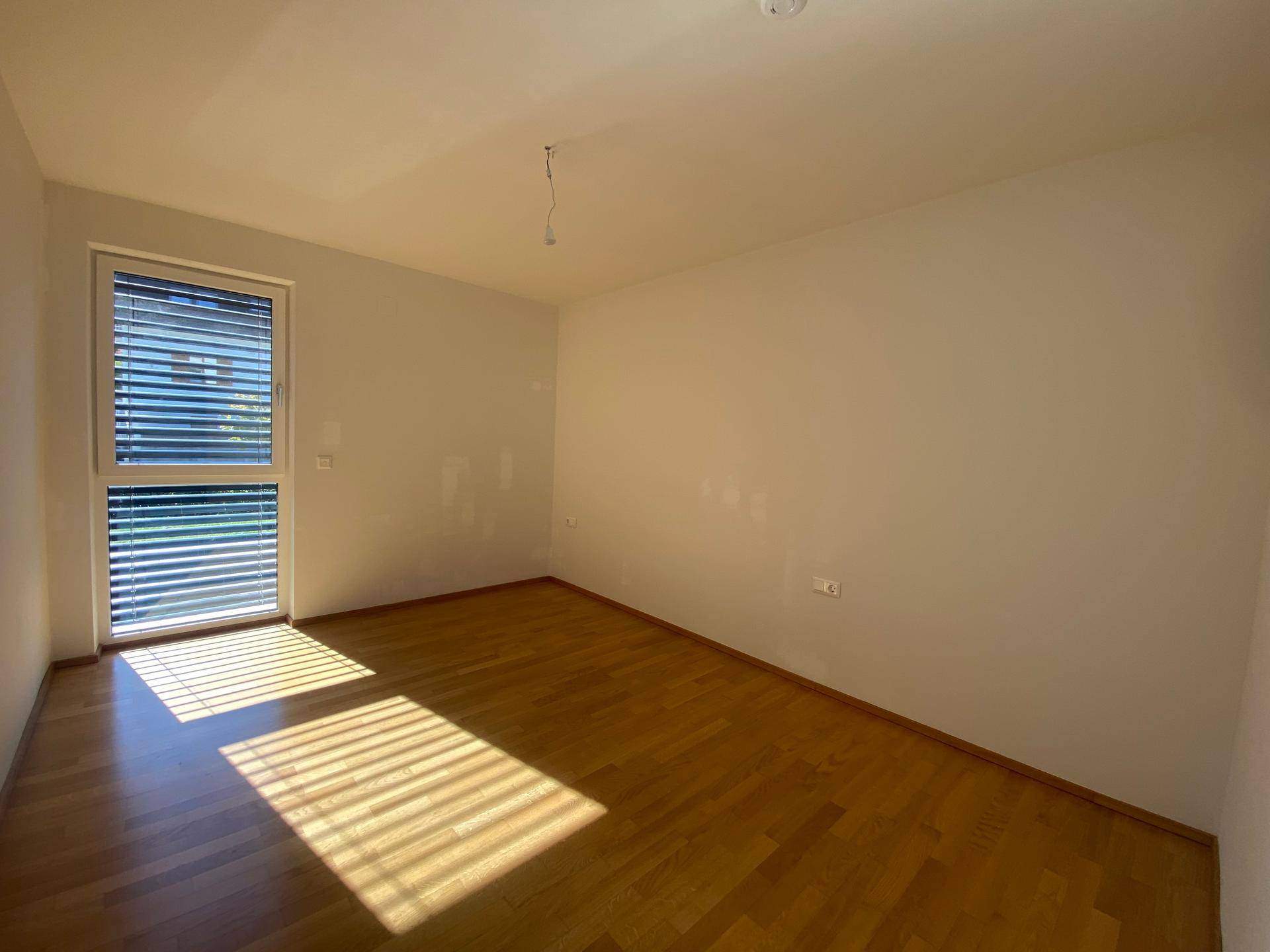 Helles Schlafzimmer mit Holzboden und großem Fenster, das viel Sonnenlicht hereinlässt.