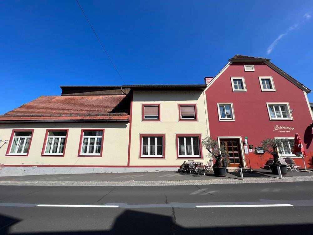 Ansicht des Gebäudes von der Straße, mit roter und beiger Fassade unter blauem Himmel.
