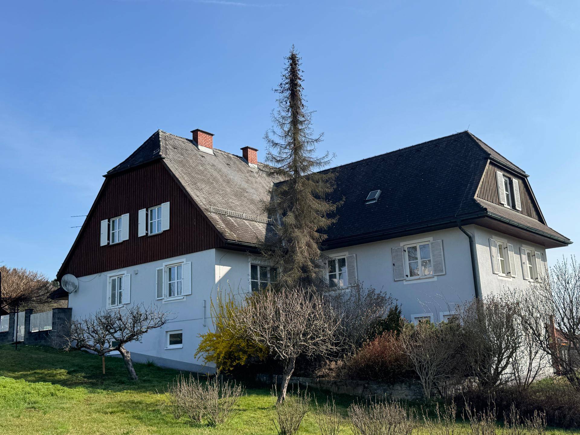 Traditionelles Wohnhaus mit Mansarddach und weiß gestrichenen Fensterläden in ländlicher Umgebung.