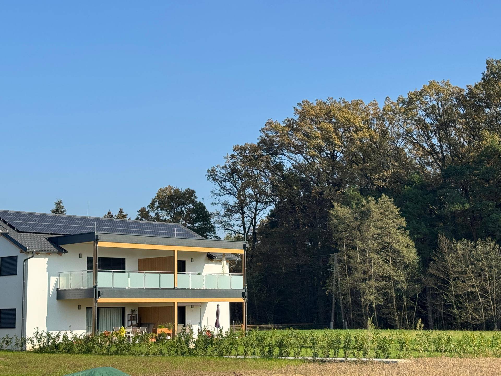 Moderne Doppelhaushälfte mit Balkon und Solaranlage, umgeben von viel Grün.