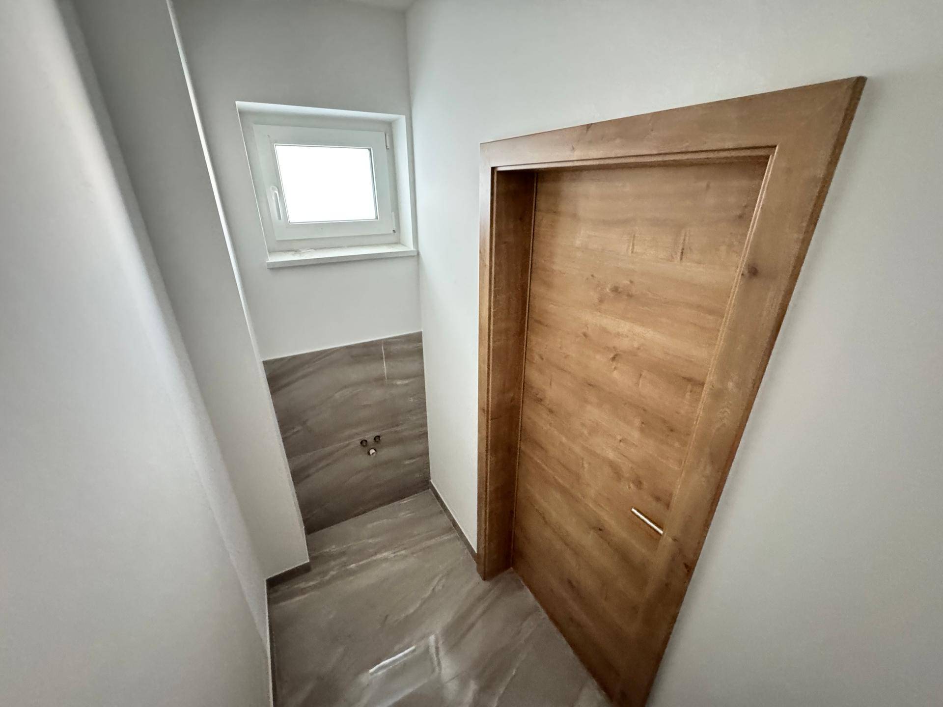 Kleines Gäste-WC mit modernen Fliesen, Fenster und vorbereiteten Anschlüssen.