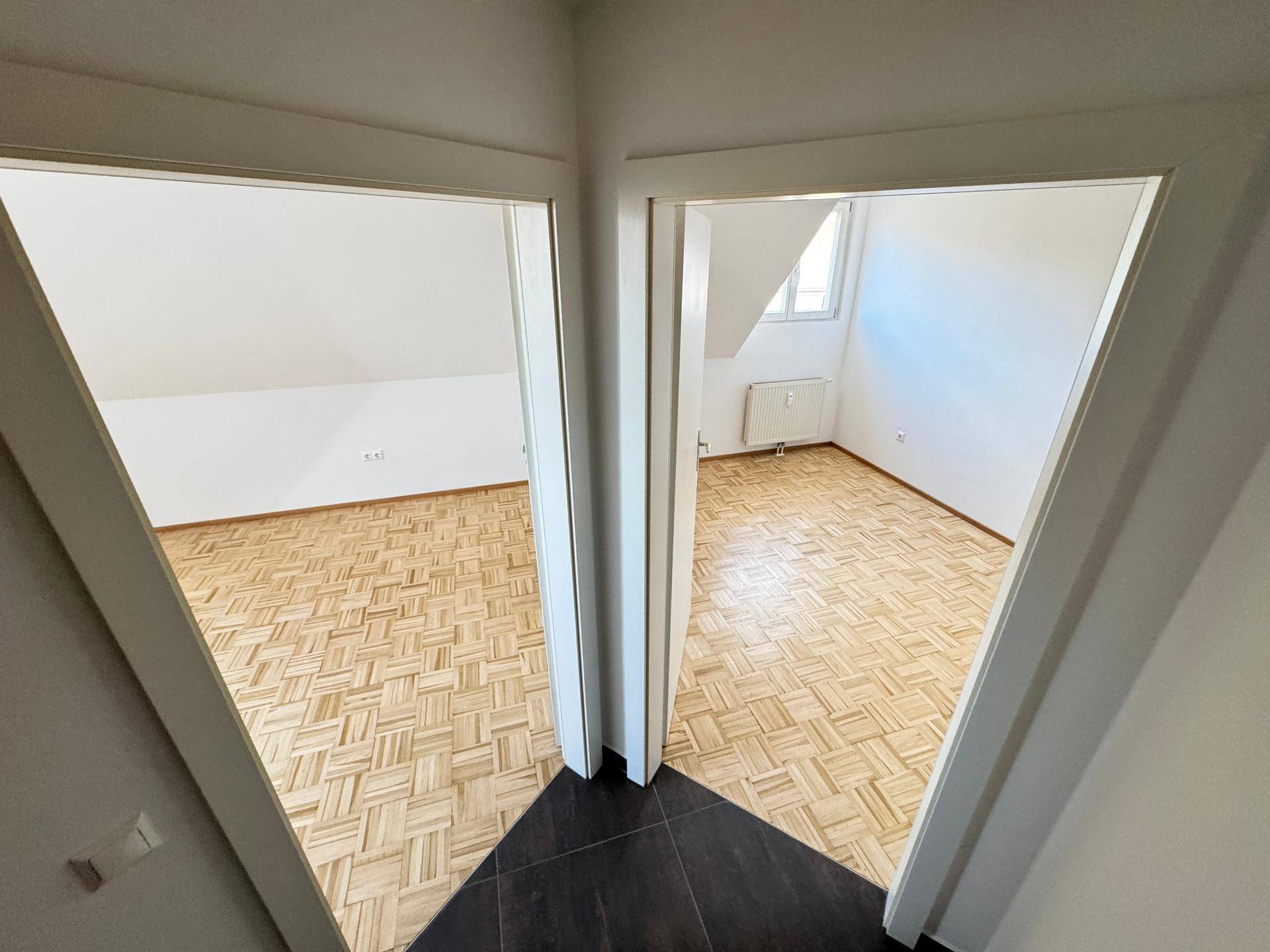 Heller Flur mit dunklen Fliesen und Blick in zwei leere Zimmer mit Parkettboden.