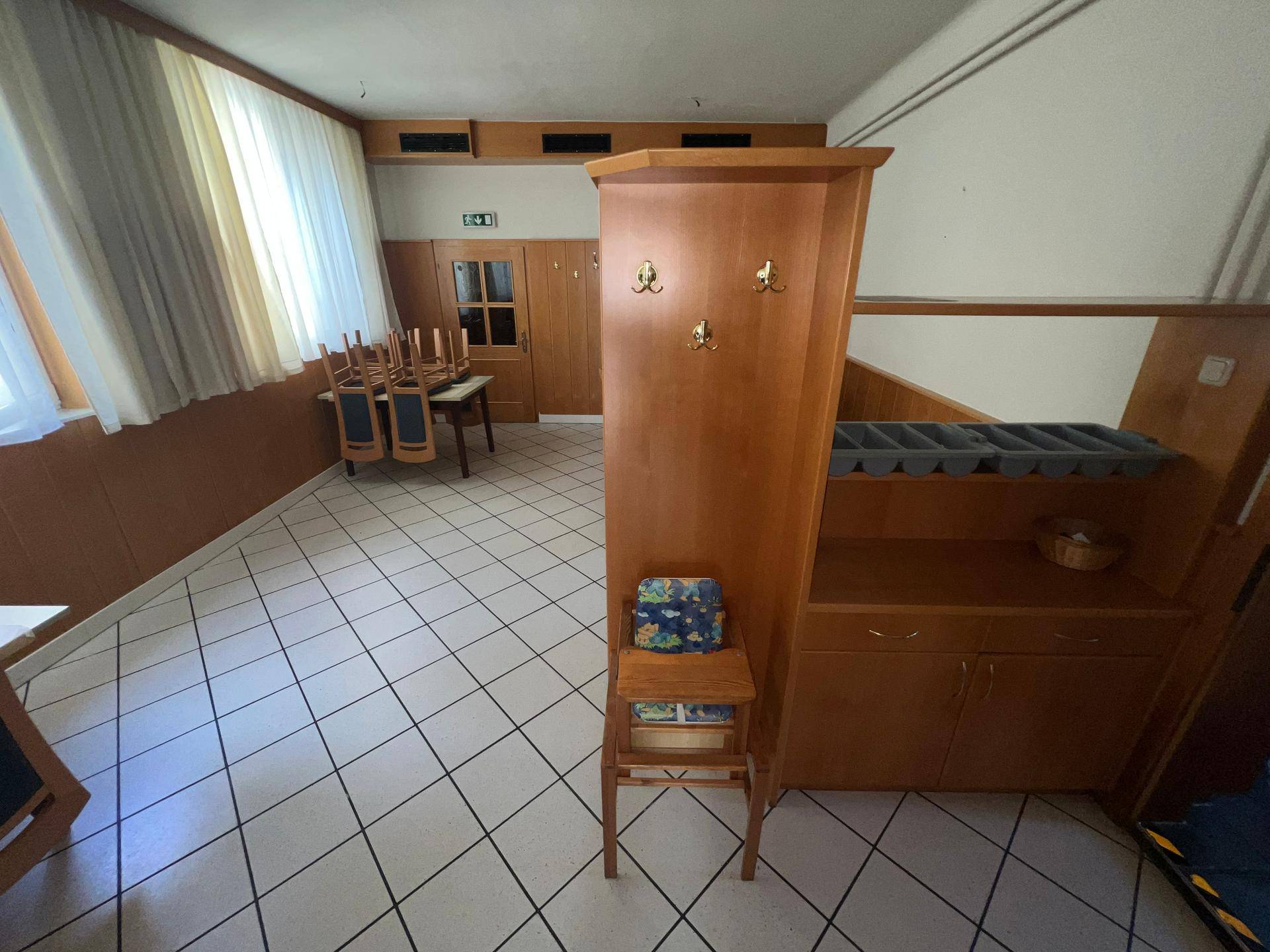 Eingangsbereich mit Fliesenboden, Holzmöbeln und Garderobe, gut beleuchtet durch Fenster.