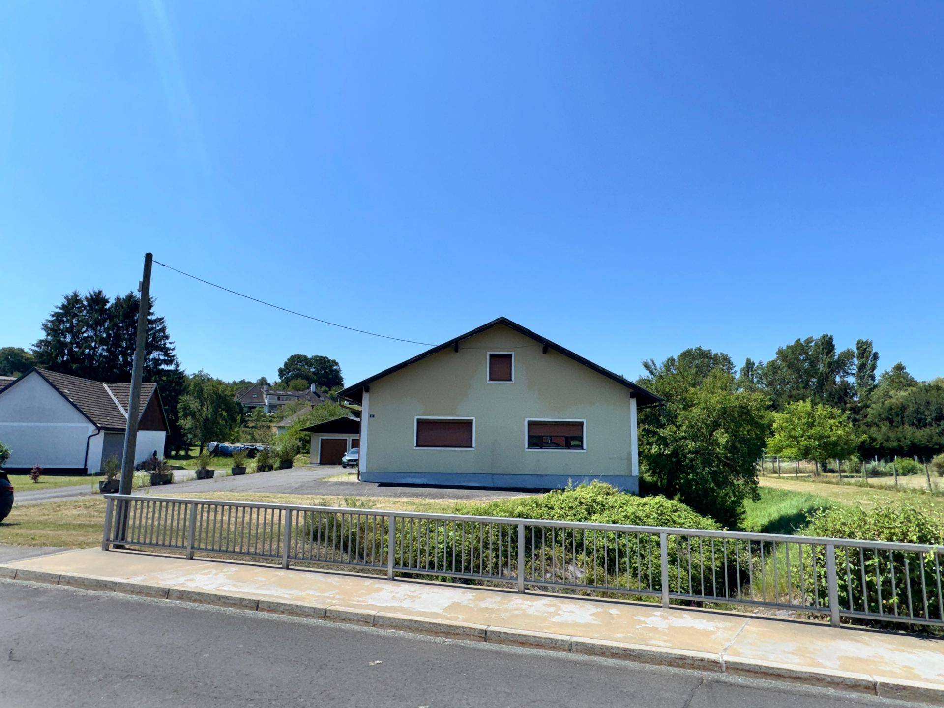 Hausansicht von der Straße mit Brücke und grüner Umgebung.