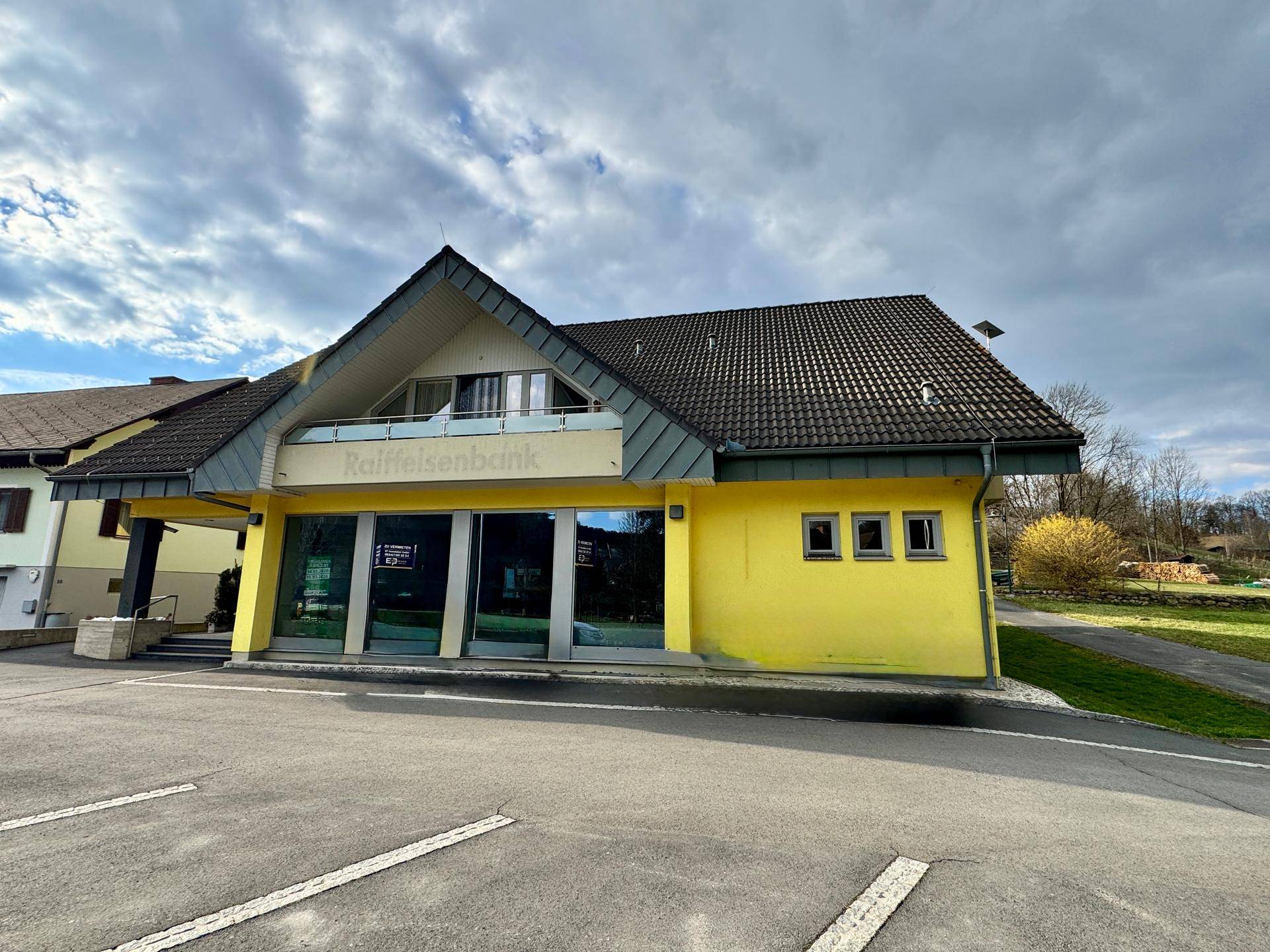 Frontale Ansicht des gelben Gebäudes mit Parkplatz und großen Fenstern.