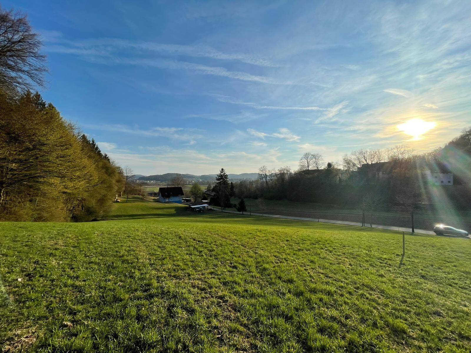 Weitläufige grüne Landschaft mit Feldern und Wäldern unter einem strahlend blauen Himmel bei Sonnenuntergang.