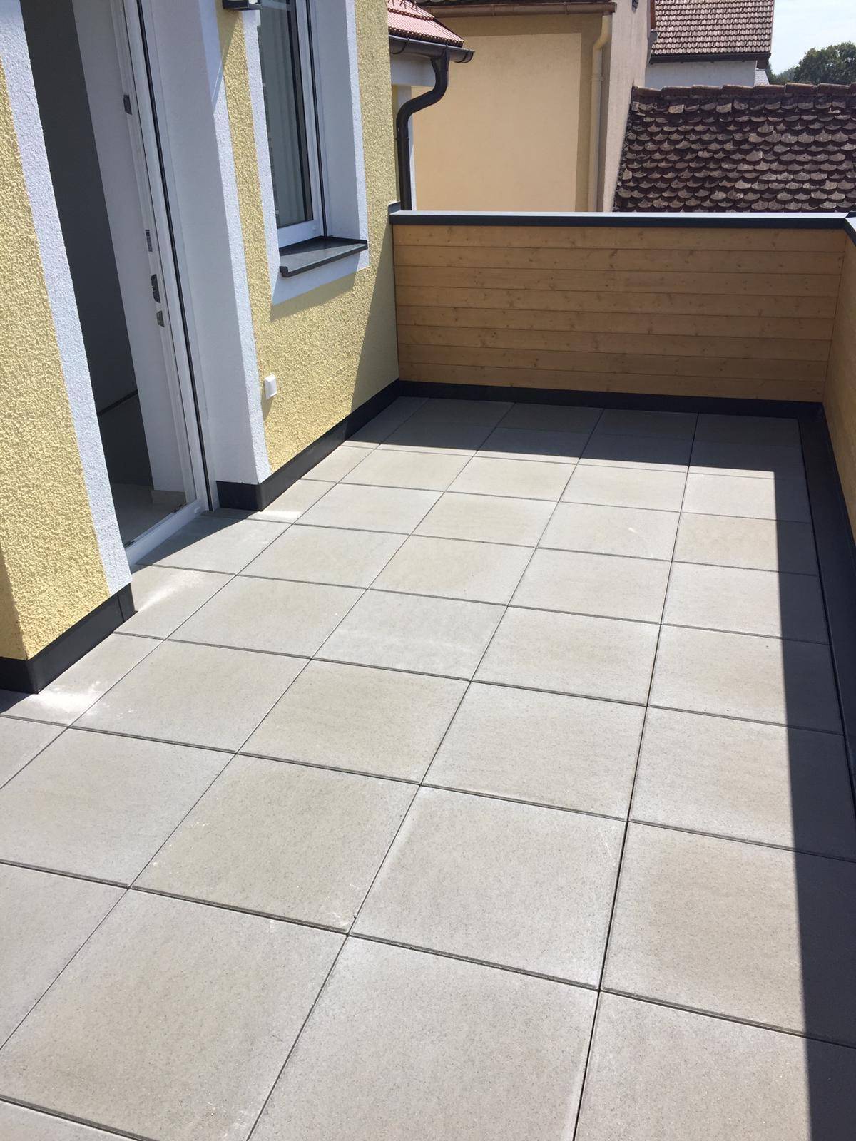 Helle Terrasse mit großen Fliesen und Holzsichtschutz, ideal für entspannte Stunden.