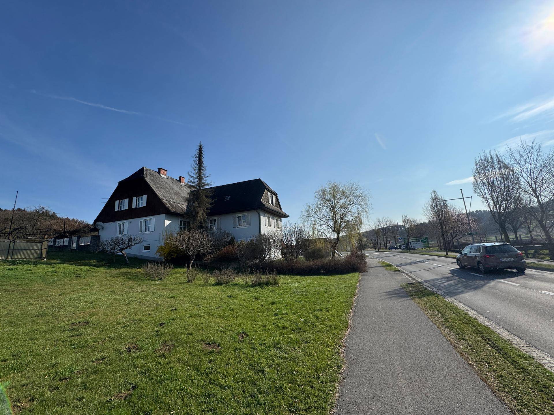 Haus mit großem Grundstück und angrenzender Straße unter strahlend blauem Himmel.