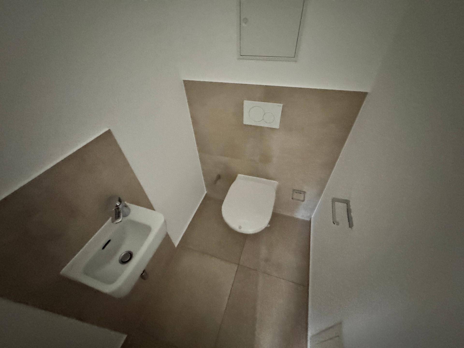 Modernes Gäste-WC mit Wand-WC, kleinem Waschbecken und beigefarbenen Fliesen.