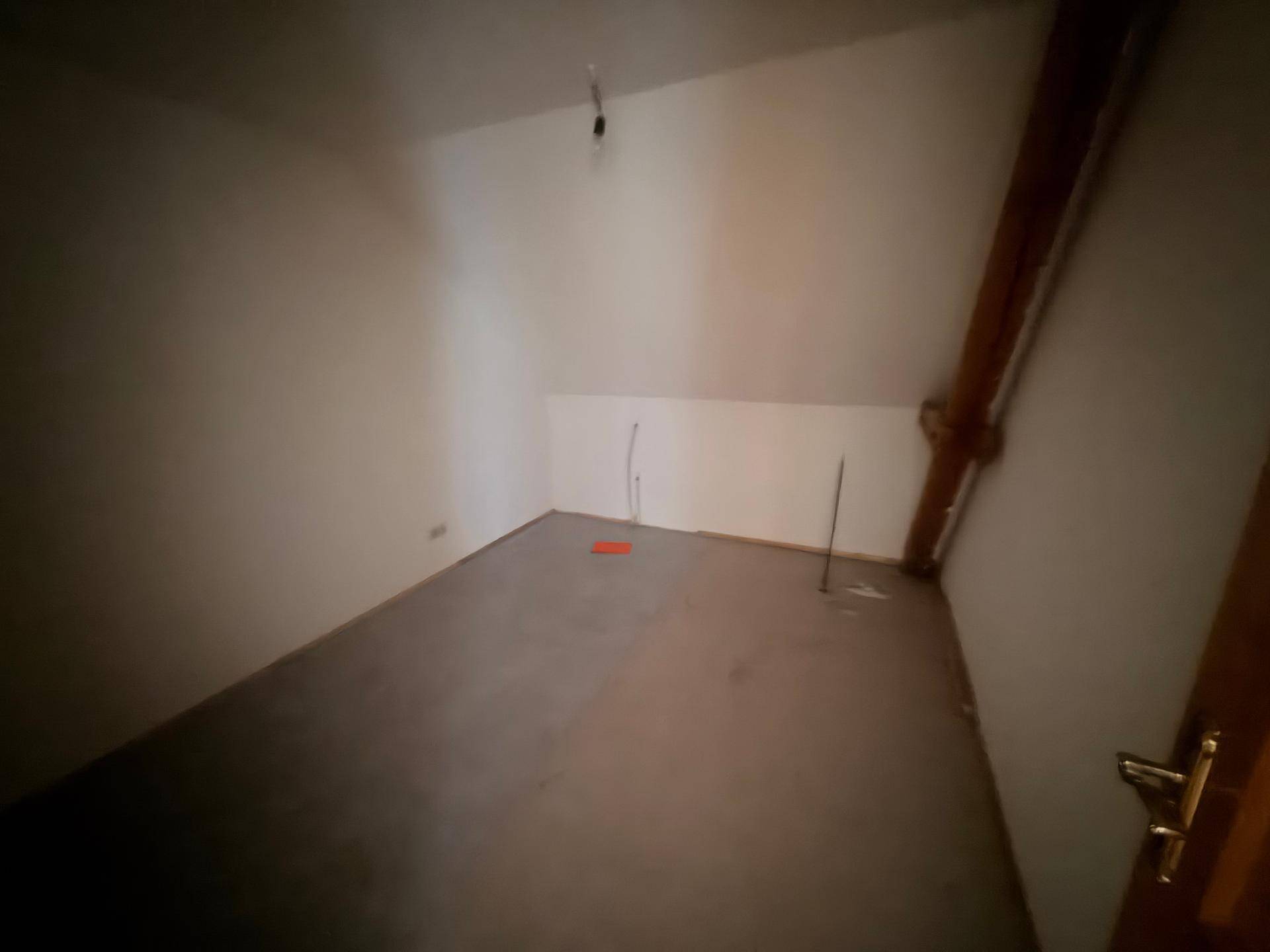 Leerer Raum im Dachgeschoss mit schrägen Wänden und einfacher Ausstattung.