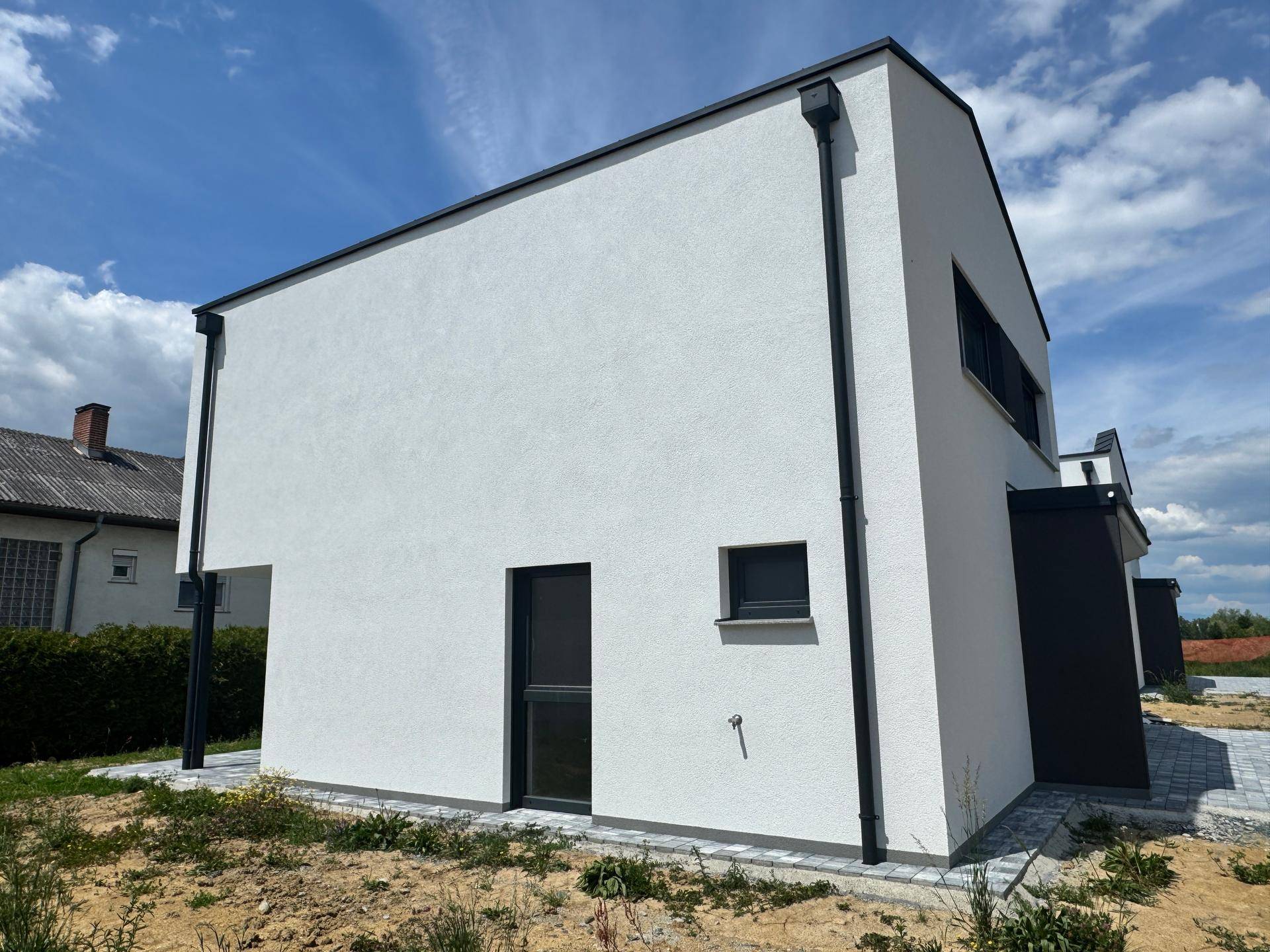 Rückansicht des modernen Neubaus mit weißer Fassade und schlichten dunklen Fenstern.