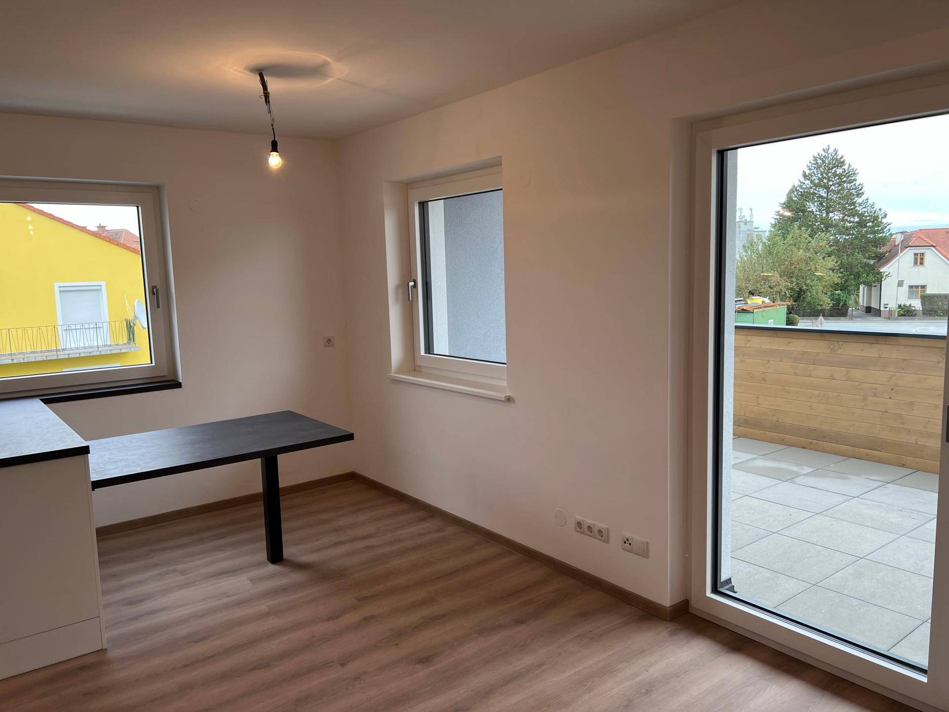 Heller Wohnbereich mit Laminatboden, großen Fenstern und Zugang zu einer Terrasse.