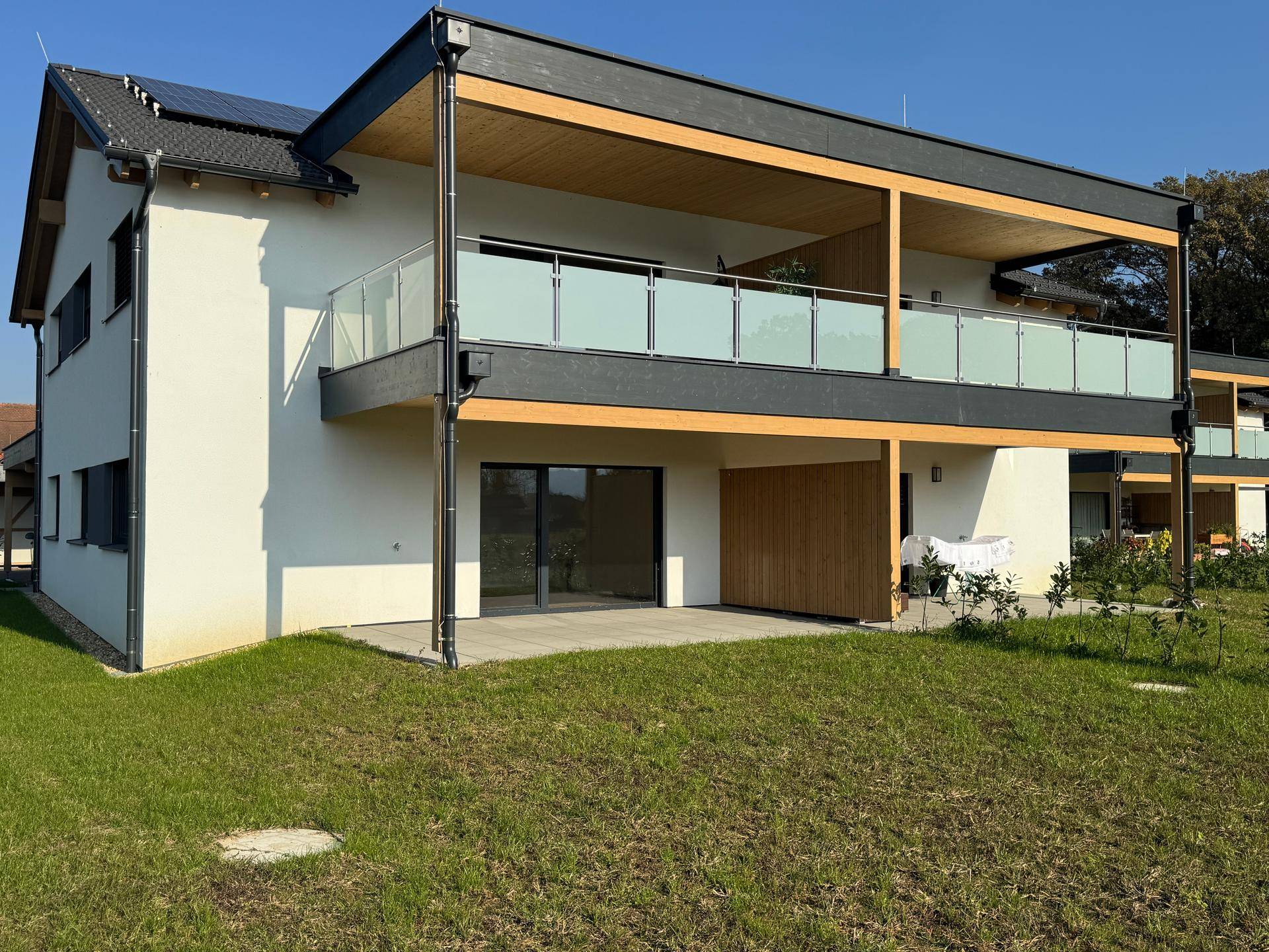 Modernes Mehrfamilienhaus mit Balkonen, Terrassen und Photovoltaikanlage auf dem Dach, umgeben von Grünflächen.