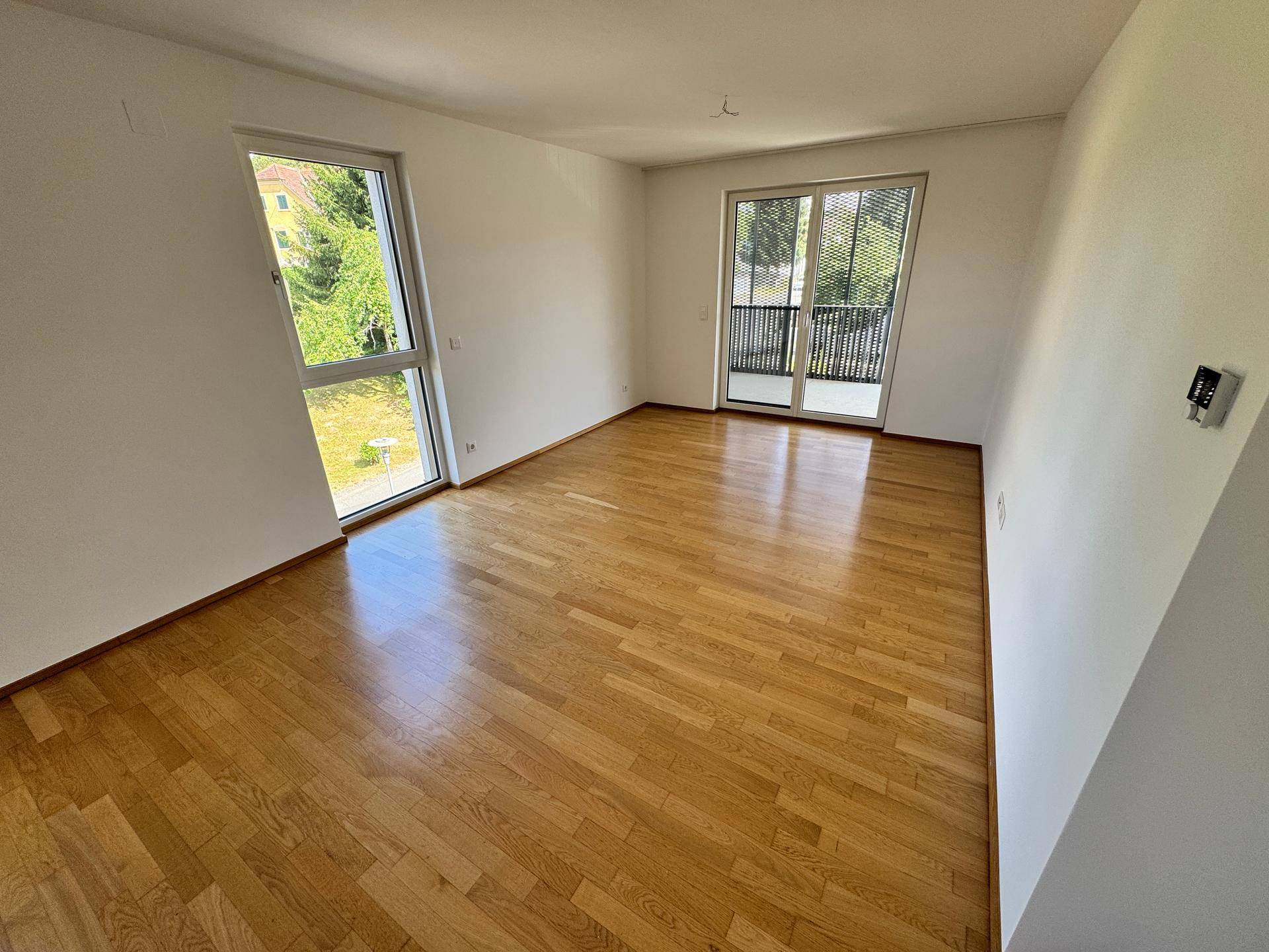Geräumiger, heller Raum mit Holzboden und großen Fenstern, die viel Tageslicht hereinlassen.