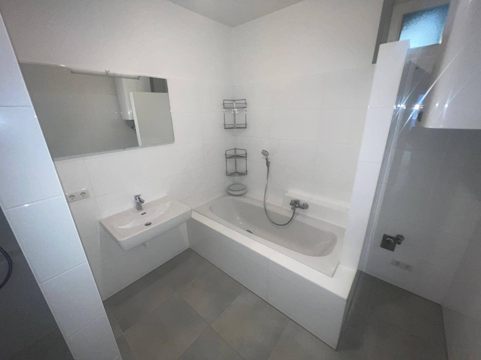 Modernes Badezimmer mit Badewanne, Dusche, Waschbecken und grauen Bodenfliesen.