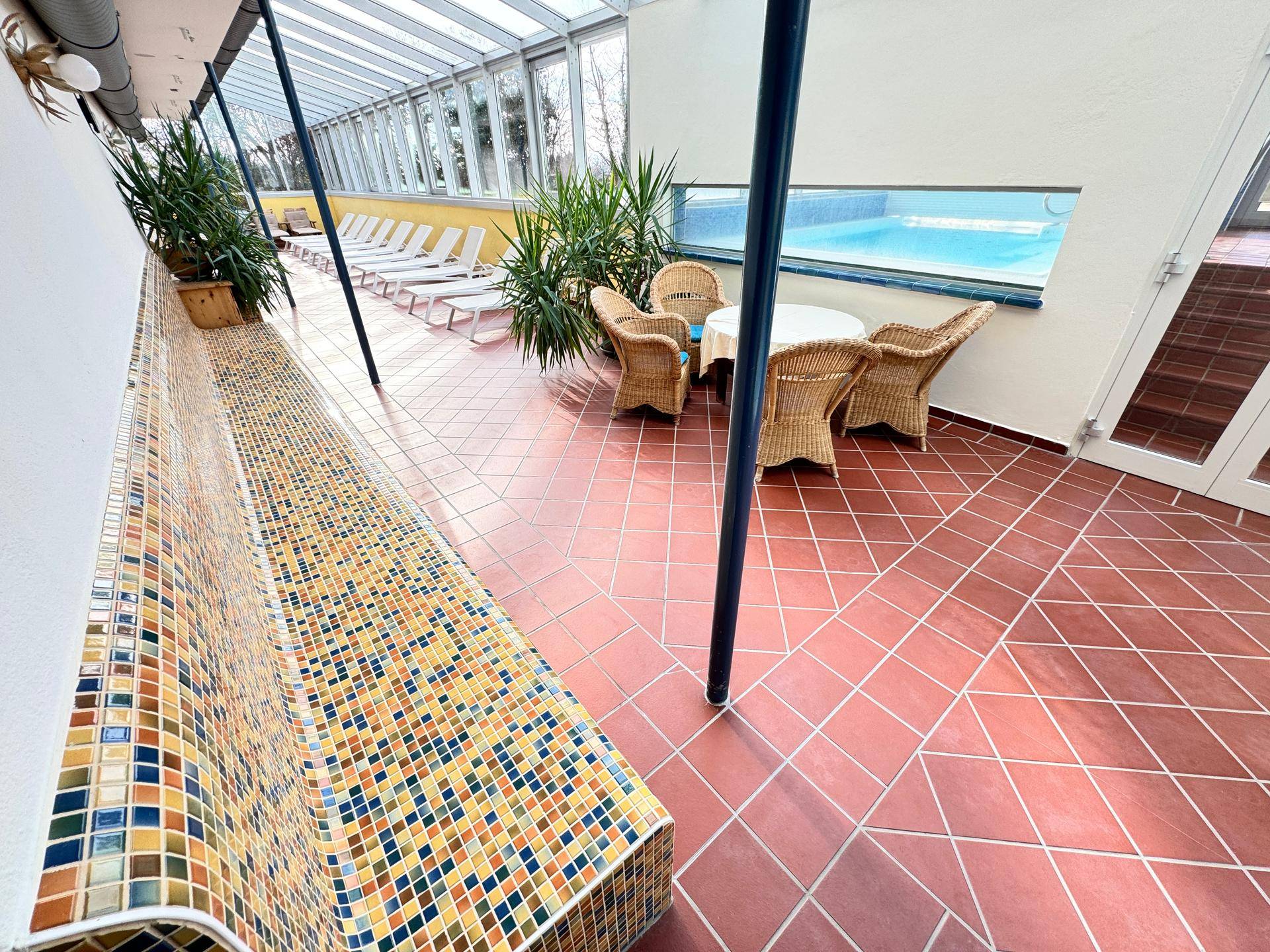 Innenpoolbereich mit Sitzgelegenheiten und großen Glasflächen.
