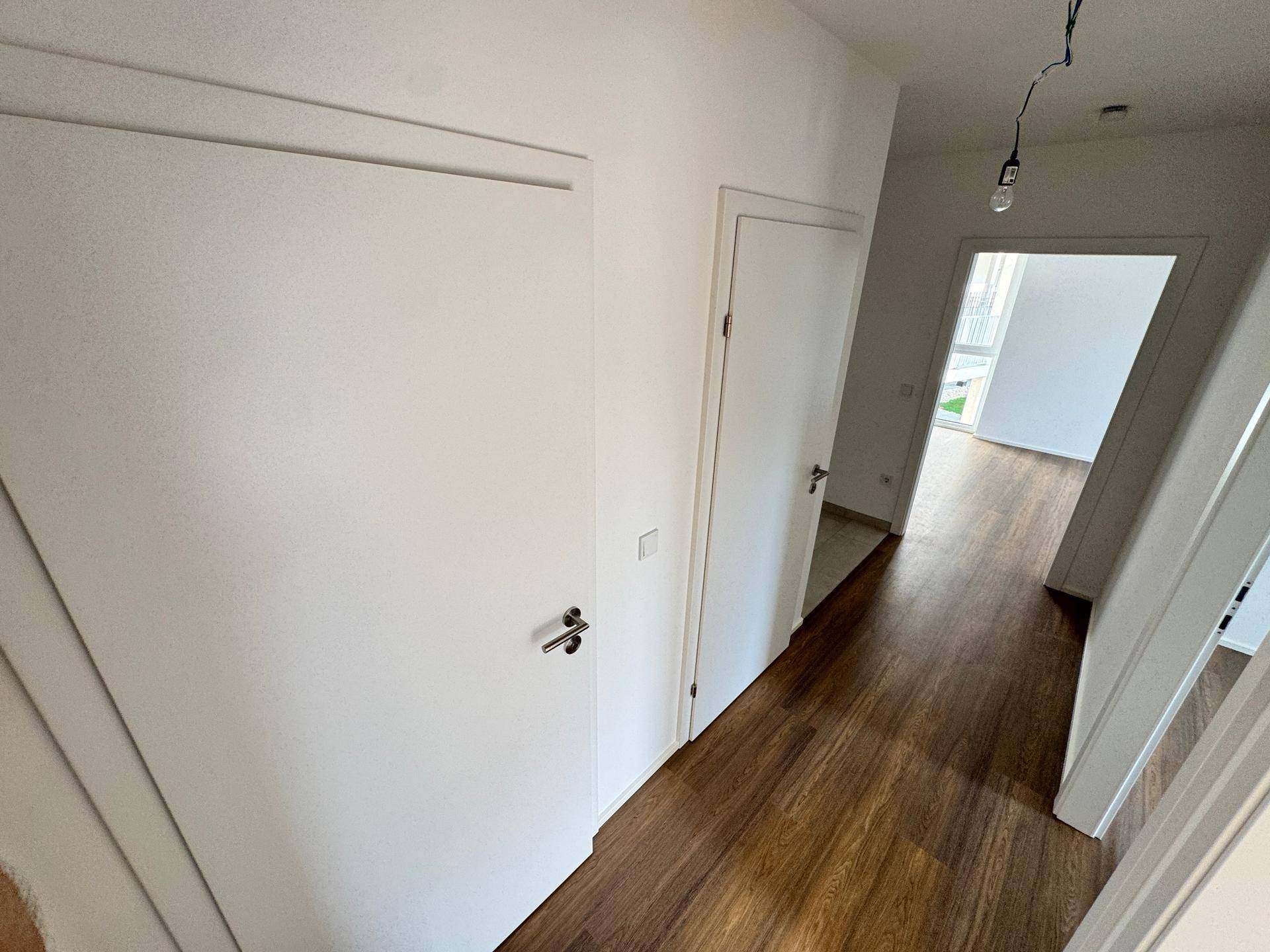 Heller Flur mit Holzboden und weißen Türen, der zu verschiedenen Zimmern der Wohnung führt.