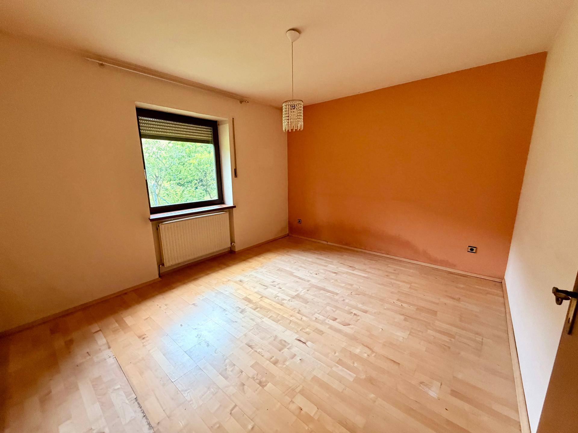 Leeres Schlafzimmer mit Laminatboden, Heizkörper und Fenster mit Rollladen.