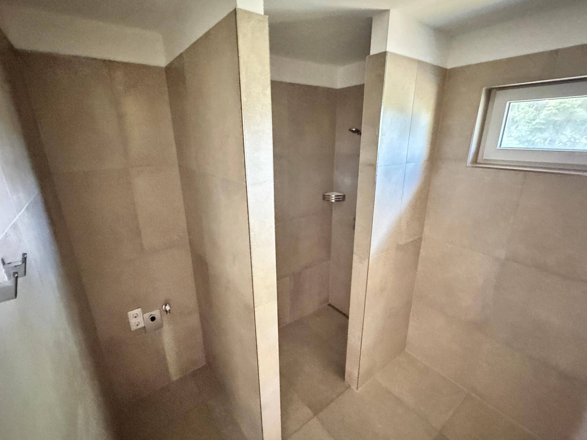 Geräumige Dusche mit beigefarbenen Fliesen und Platz für eine Waschmaschine in einem modernen Bad.