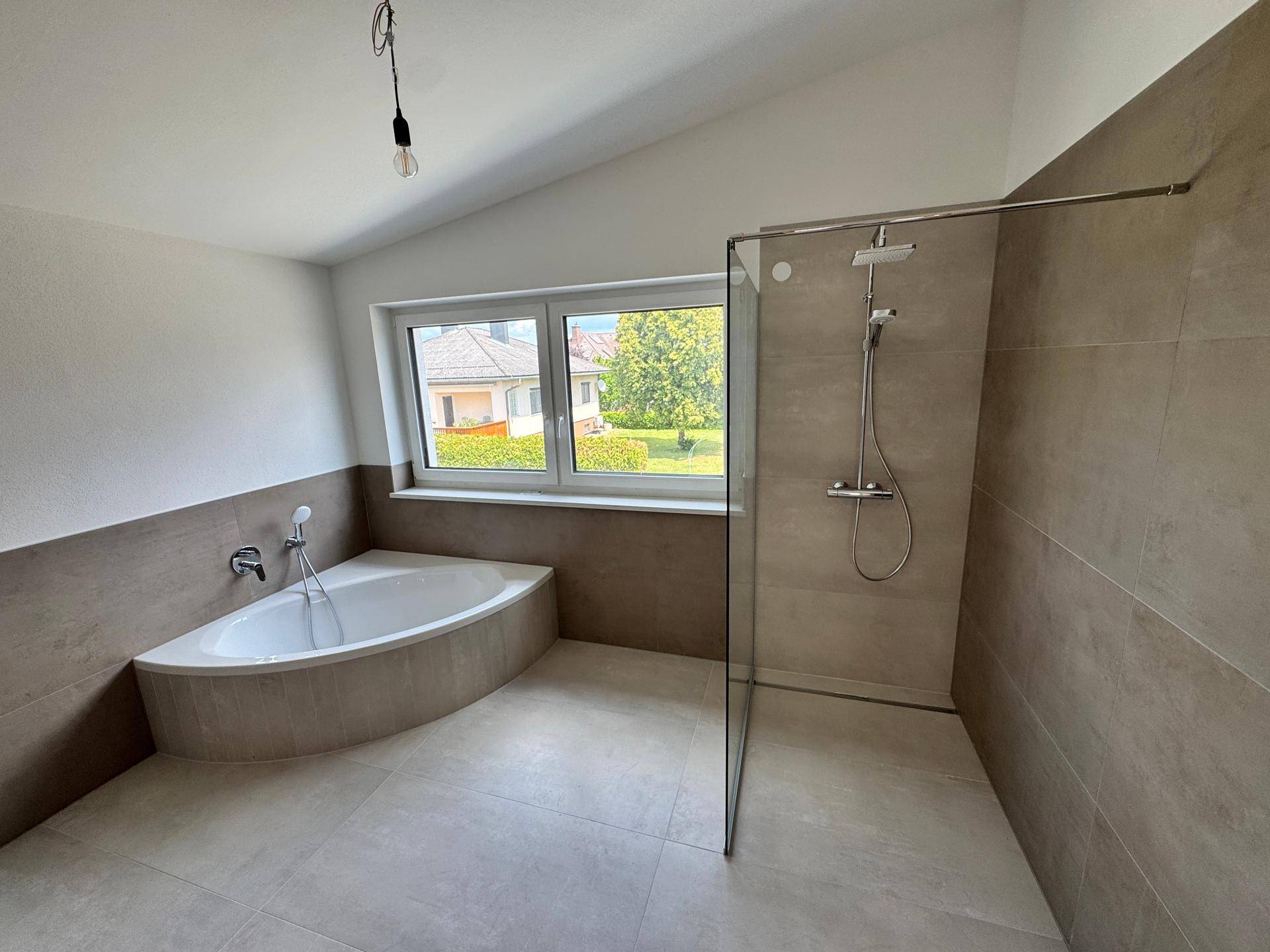 Modernes Badezimmer mit Eckbadewanne, ebenerdiger Dusche und Fenster für natürliches Licht.