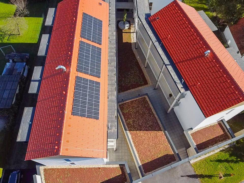 Luftaufnahme von Wohngebäuden mit roten Dächern, Solaranlagen und begrünten Innenhöfen.