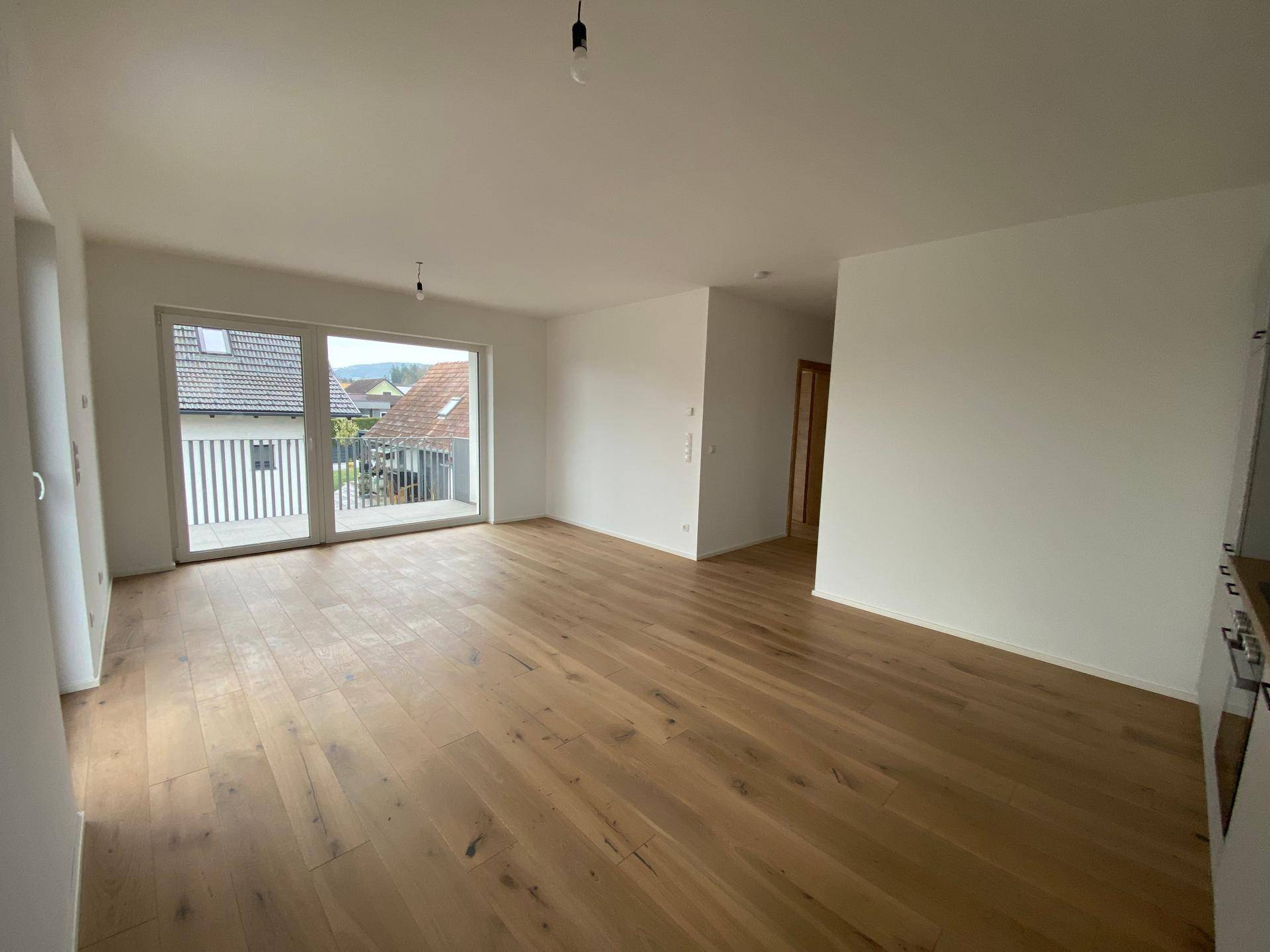 Heller Wohnbereich mit Holzboden und großen Fenstern, die viel Tageslicht hereinlassen.