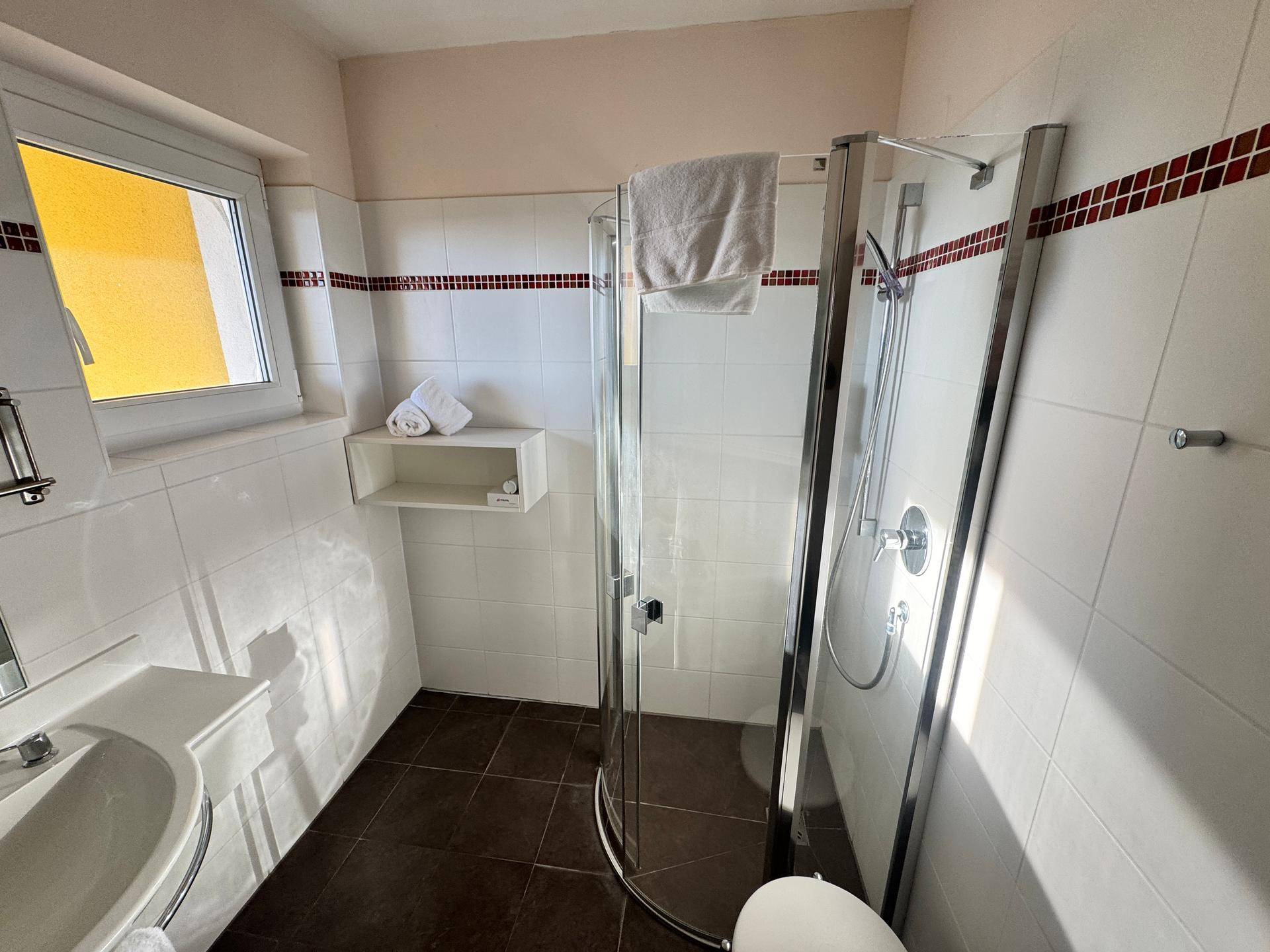 Badezimmer mit Duschkabine, Waschbecken und Fenster.