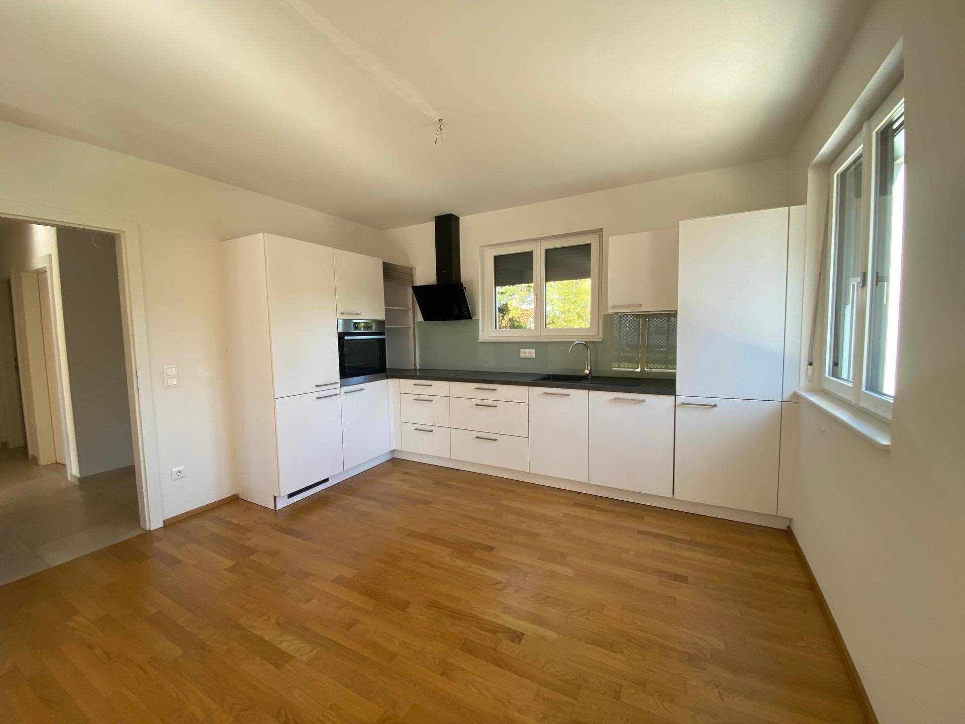 Moderne Einbauküche mit weißen Schränken, dunkler Arbeitsplatte und Fenster mit Blick ins Grüne.