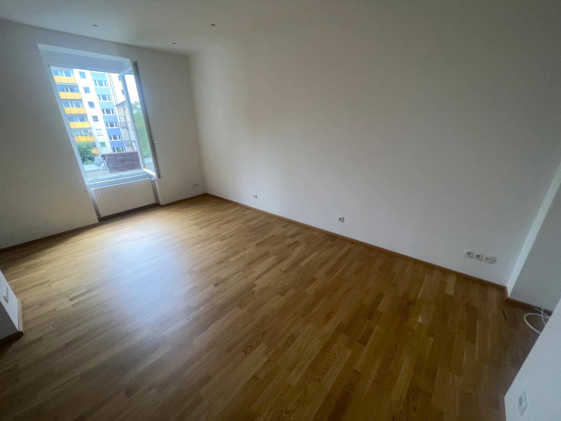 Helles Wohnzimmer mit Parkettboden und einem großen Fenster mit Blick ins Grüne.