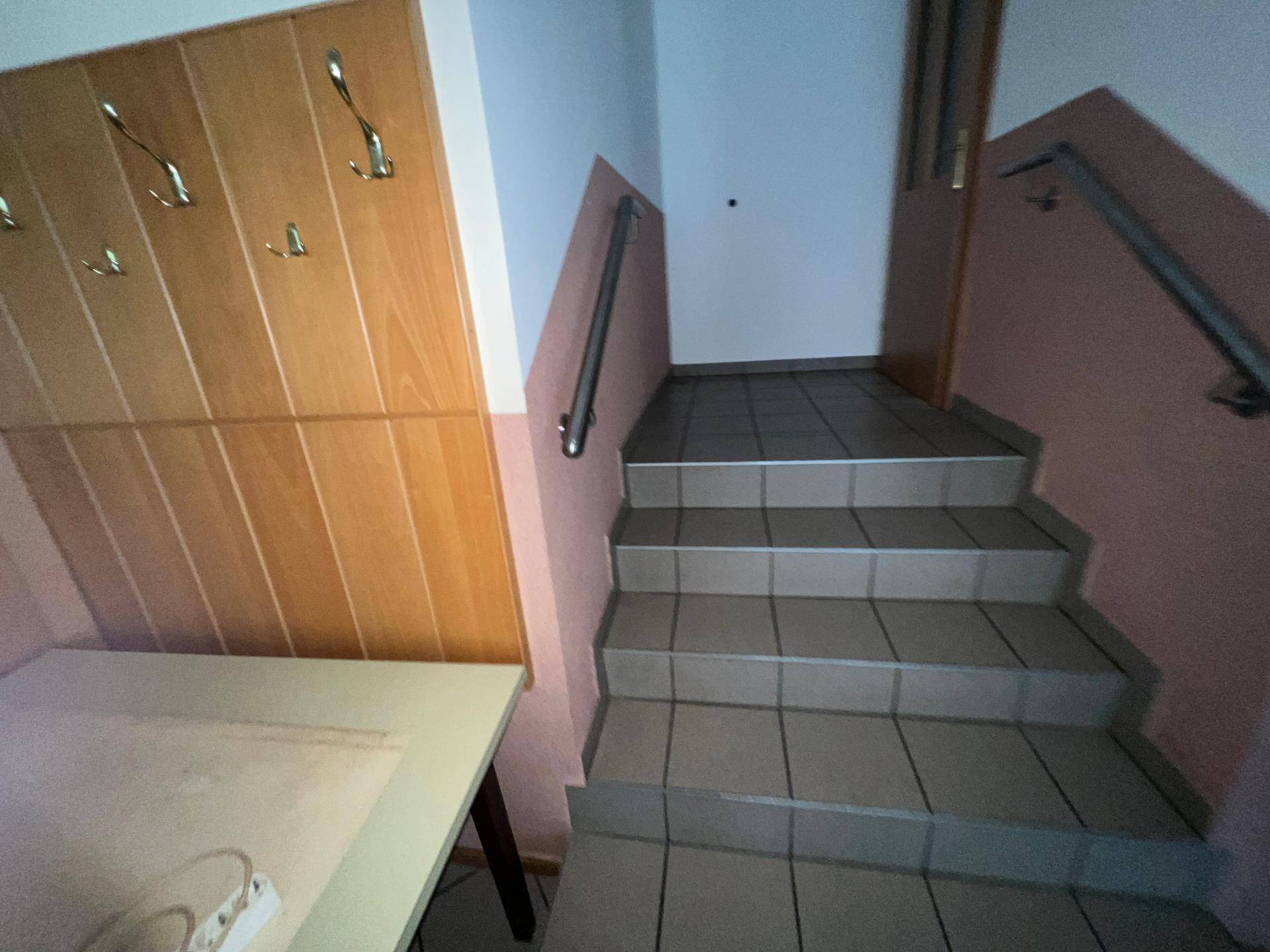 Treppenhaus mit gefliesten Stufen, Handlauf und Holzvertäfelung an der Wand.