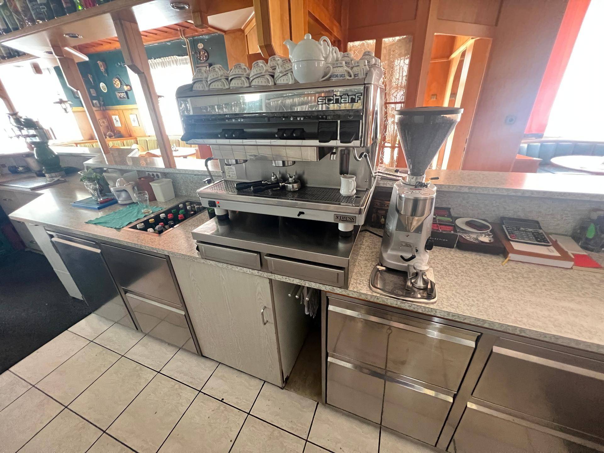Professionelle Kaffeemaschine auf einer Theke mit Edelstahlunterschränken und Fliesenboden.
