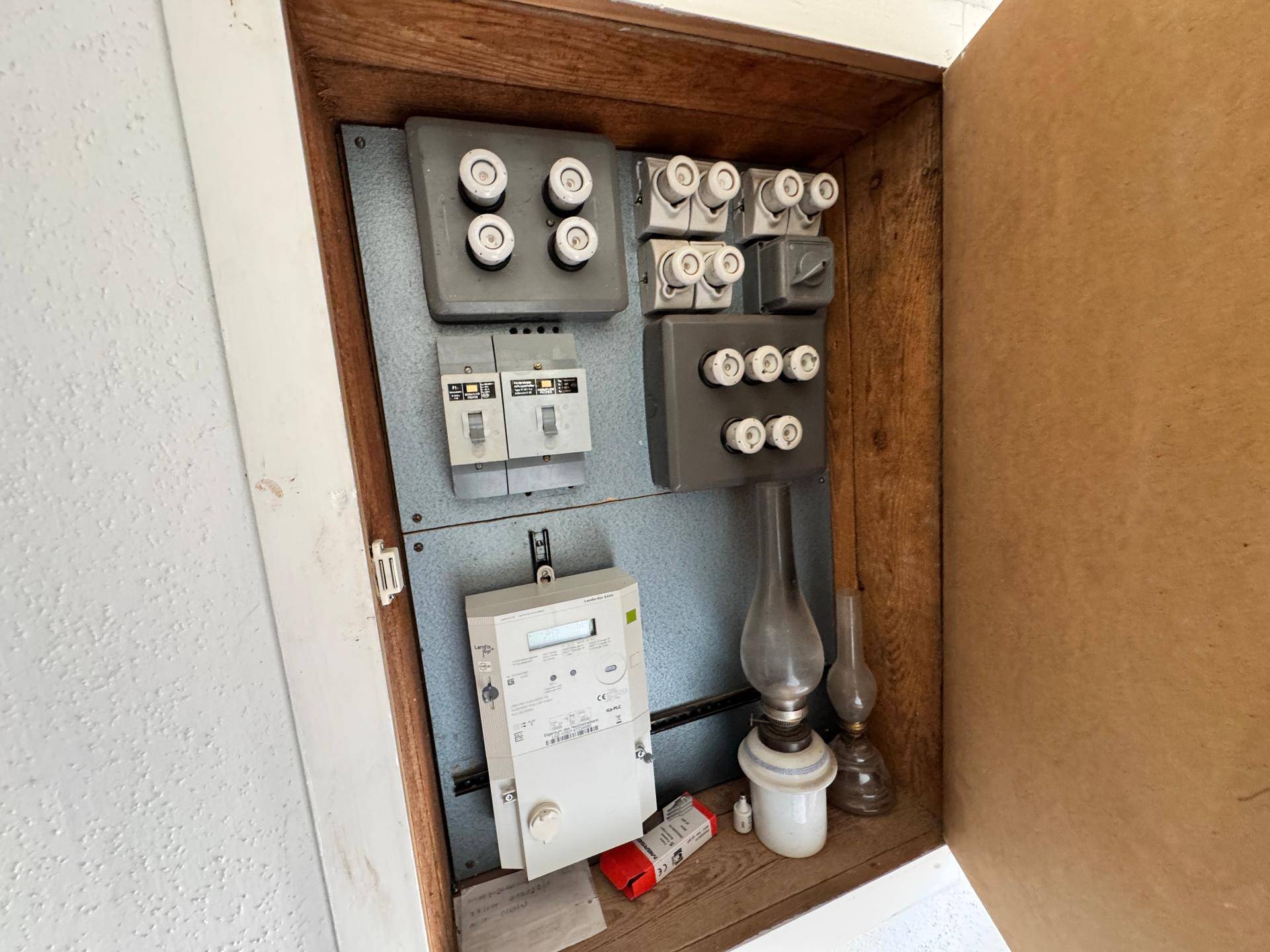 Alter Sicherungskasten mit Stromzähler und traditionellen Sicherungen in einem Holzschrank.