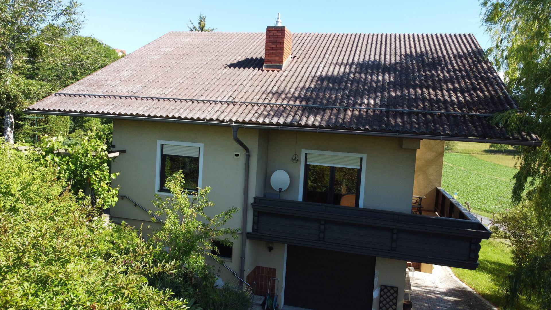 Vogelperspektive des Hauses mit Ziegeldach und Balkon, eingebettet in die Natur.