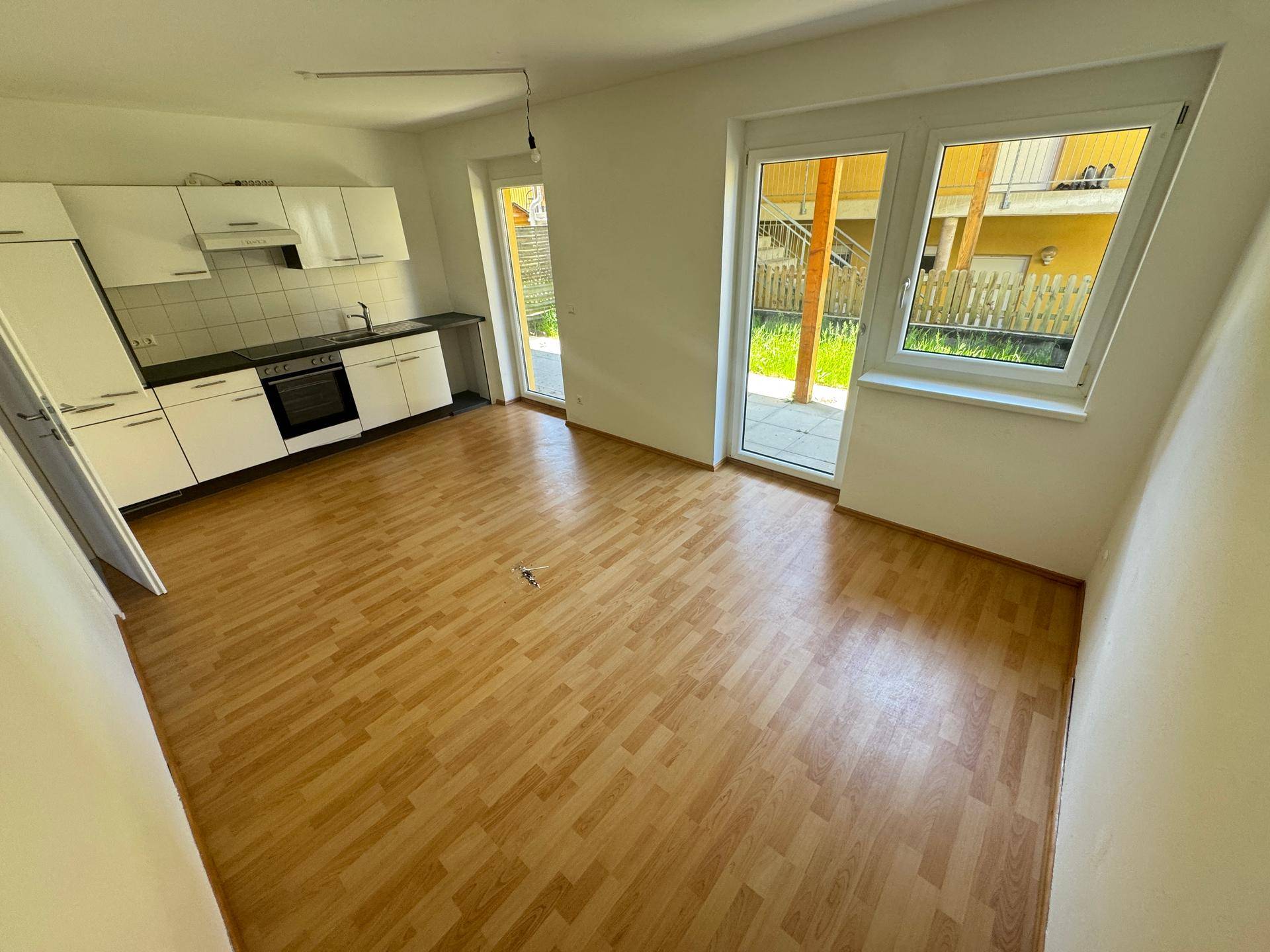 Offene Küche mit weißen Schränken, Laminatboden und Zugang zu einem Außenbereich.