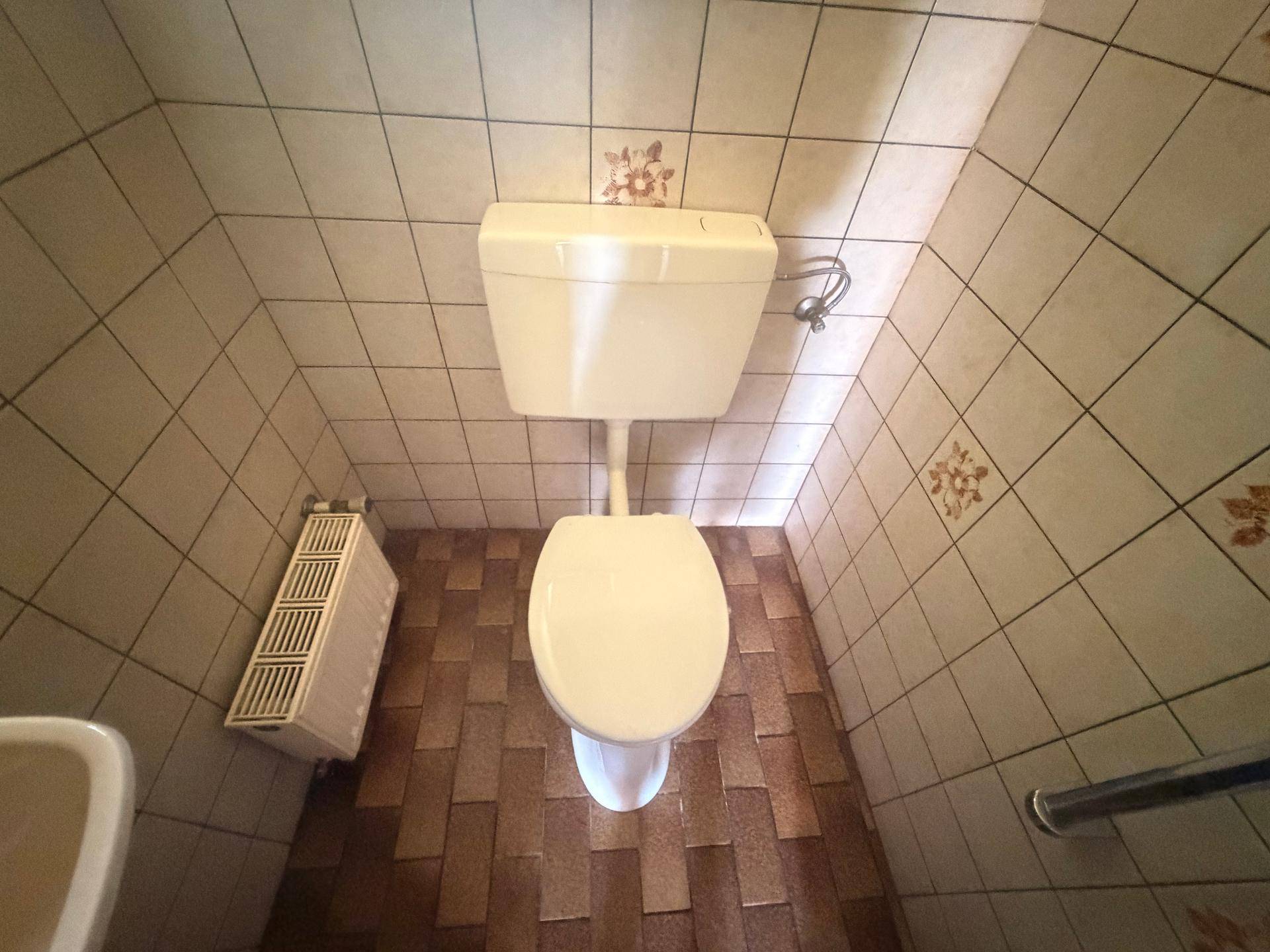 Kleines WC mit Fliesen an Wänden und Boden, ausgestattet mit einem Heizkörper.