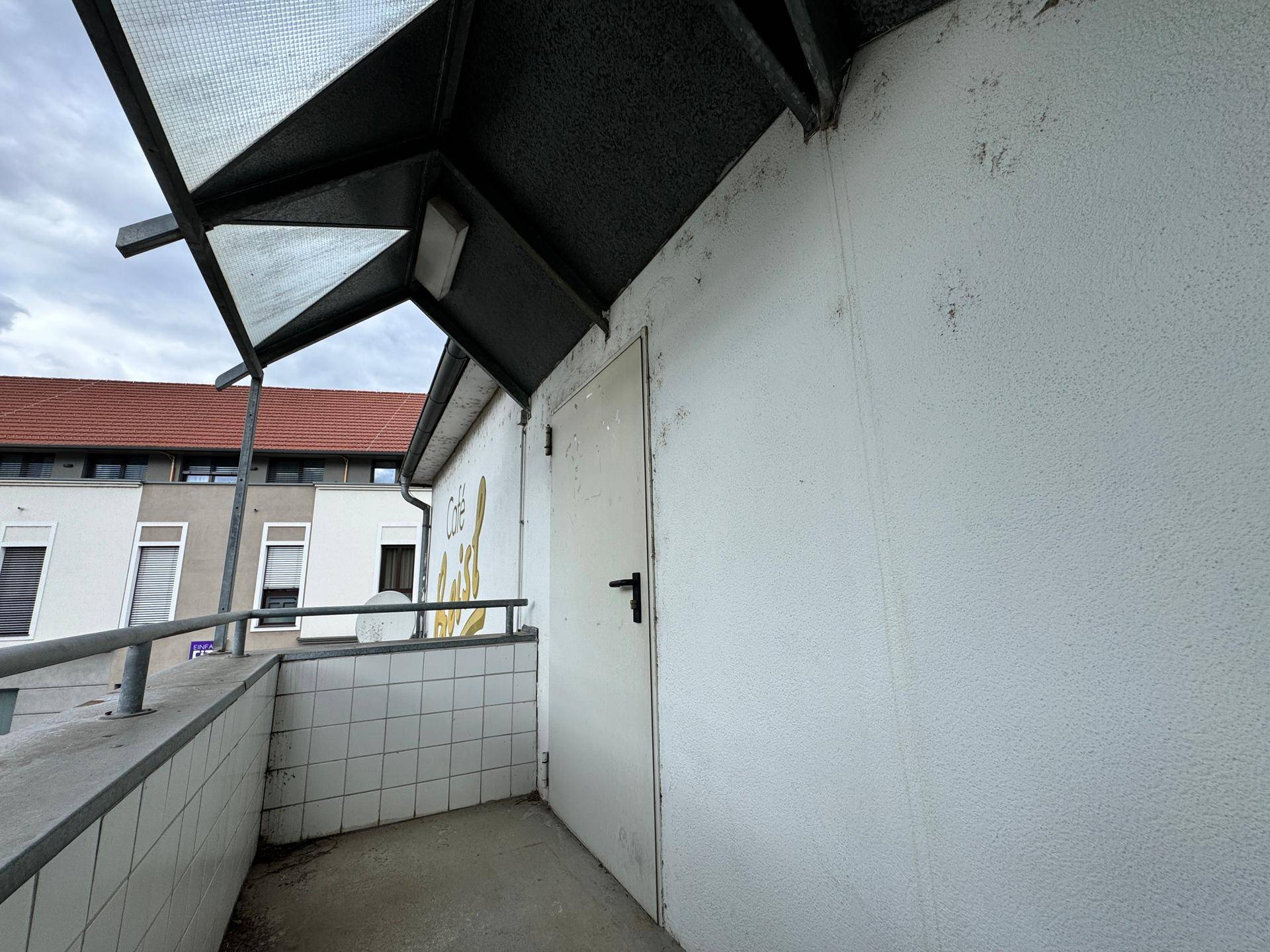 Überdachter Außenbereich mit Fliesenbrüstung und einer Tür, die zu einem Gebäude führt.