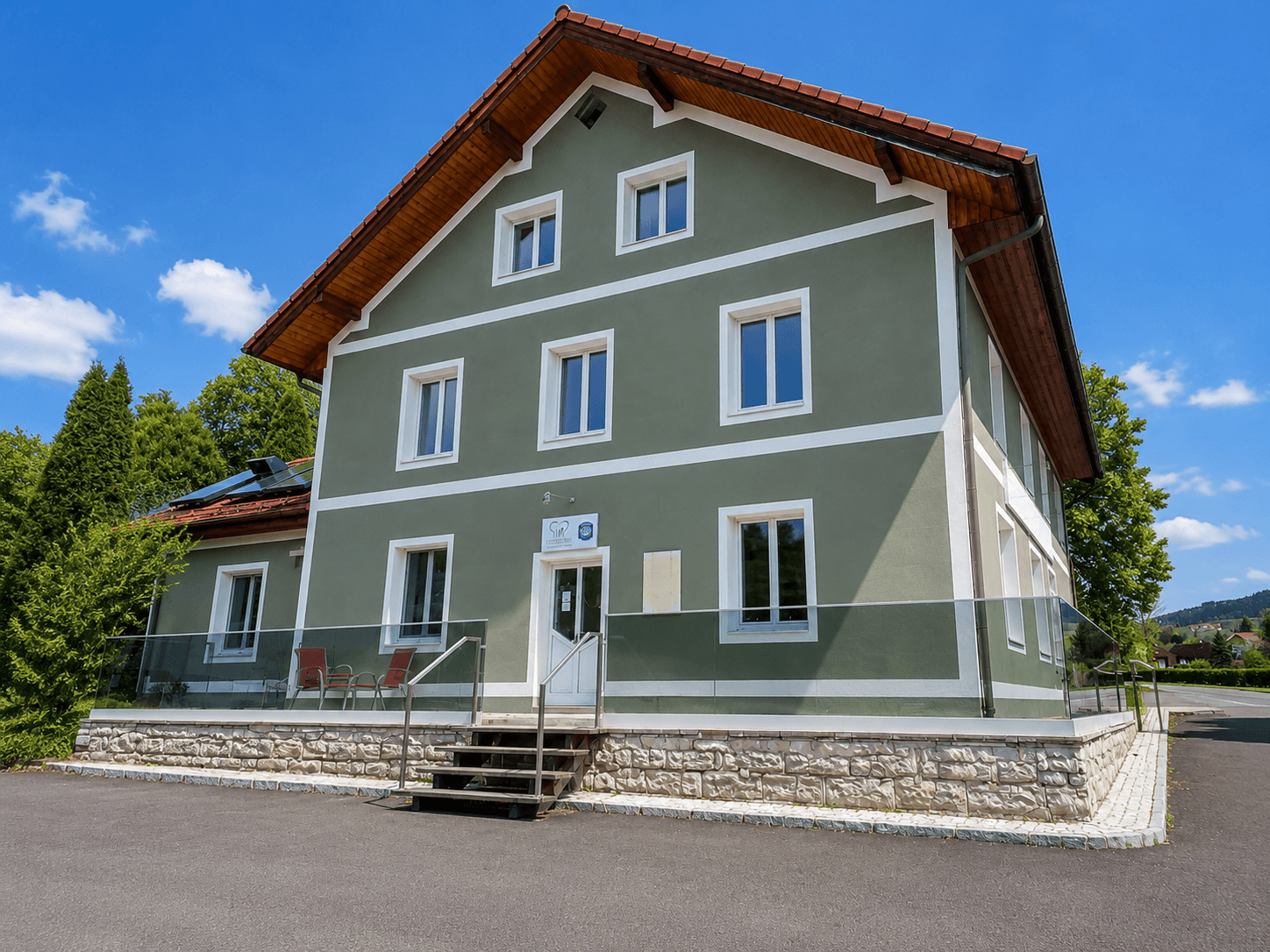 Die Rückseite des Gebäudes zeigt eine grüne Fassade, ein rotes Dach und eine kleine Terrasse mit Glasgeländer.