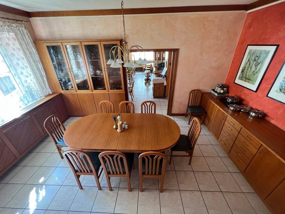 Heller Essbereich mit Holztisch, Vitrinenschrank und Zugang zu weiteren Räumen.