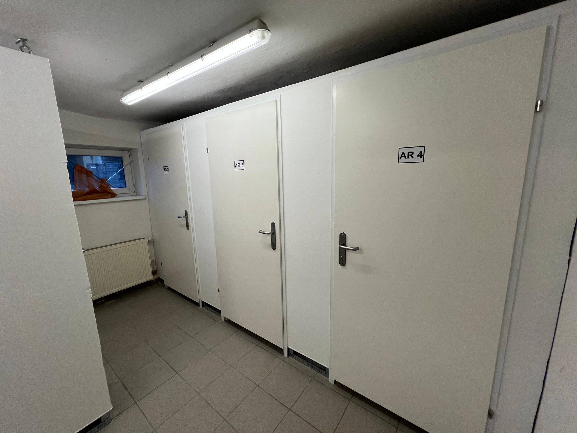 Heller Kellerraum mit mehreren weißen Lagerabteilen, Fliesenboden und einem kleinen Fenster.