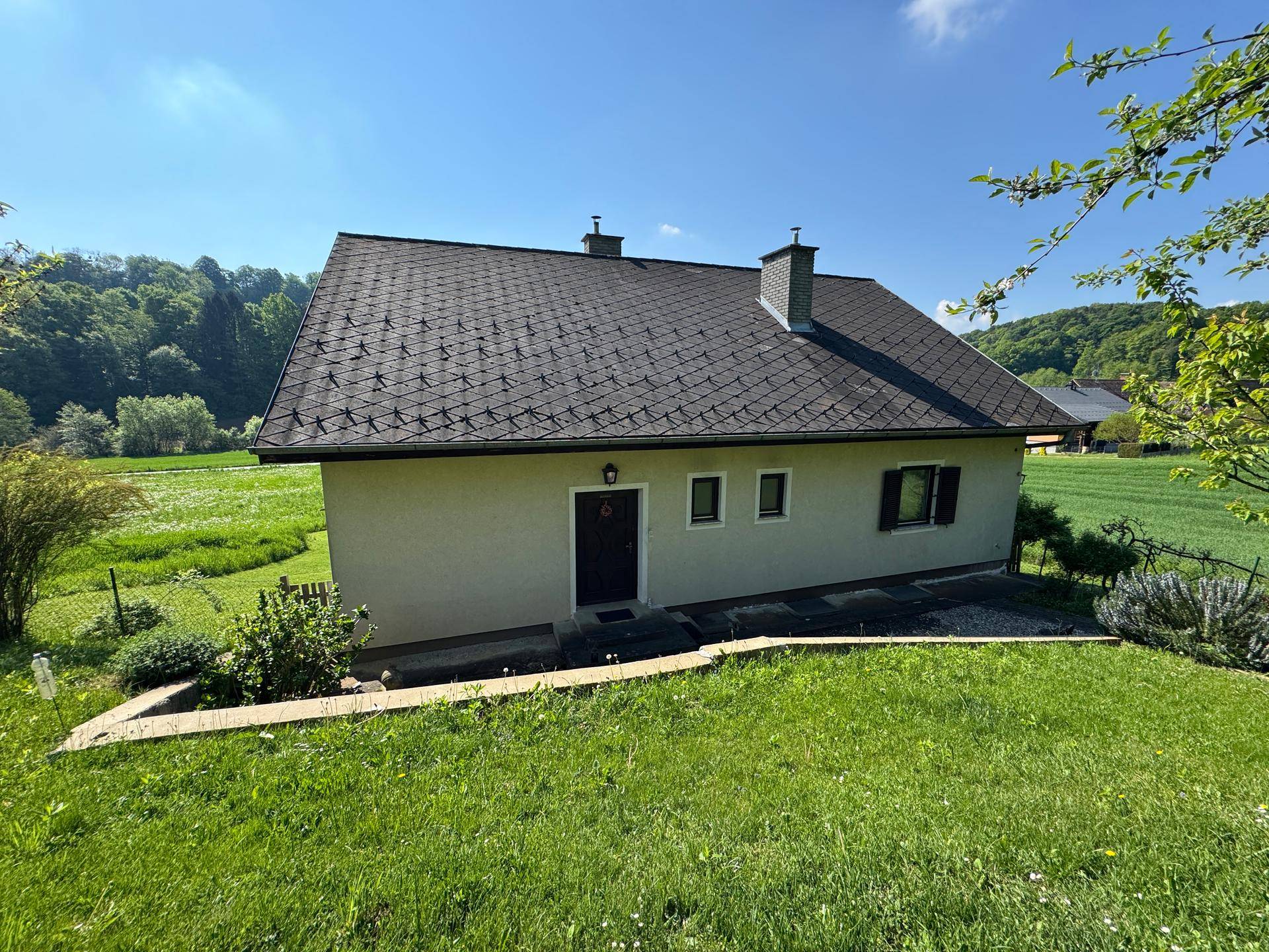 Seitenansicht des Hauses mit dunklem Ziegeldach und gepflegter Rasenfläche.