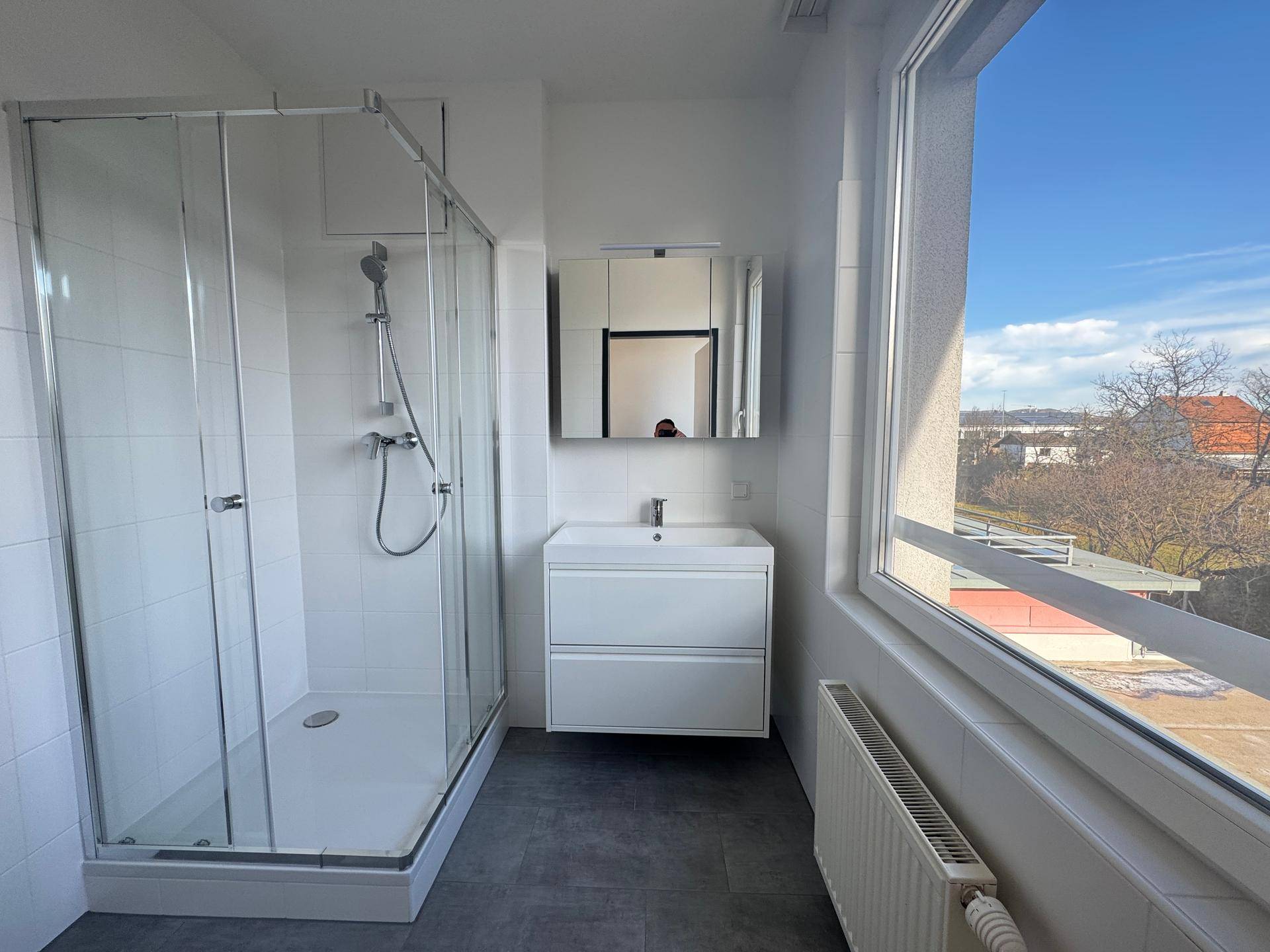 Modernes Badezimmer mit Duschkabine, Waschbecken und großem Fenster.