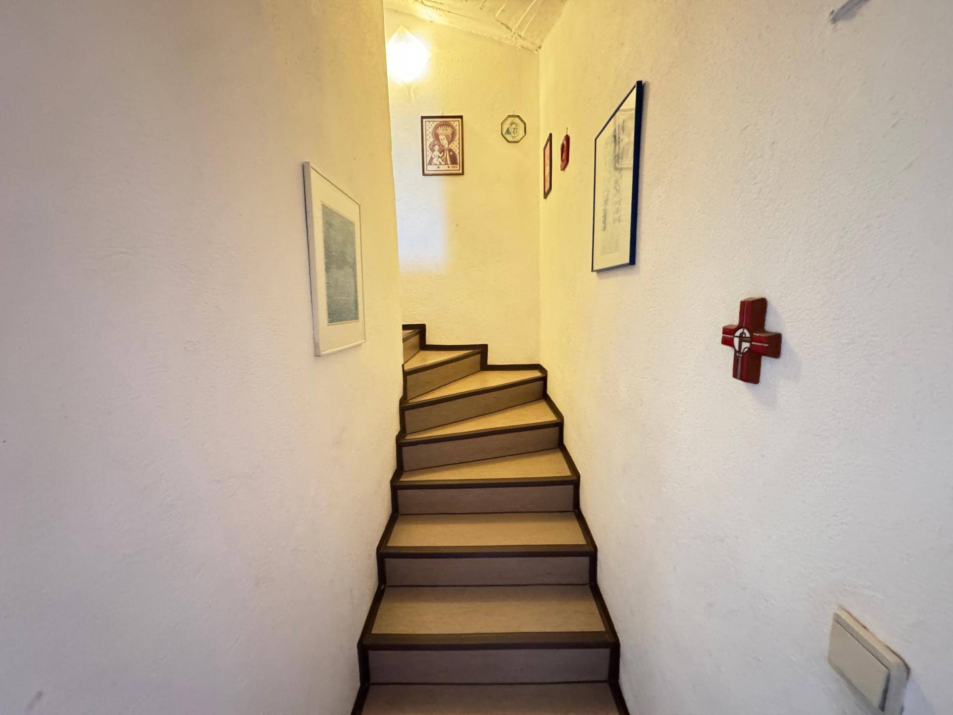 Treppenhaus mit Teppichstufen und weißen Wänden, das die verschiedenen Etagen des Hauses verbindet.