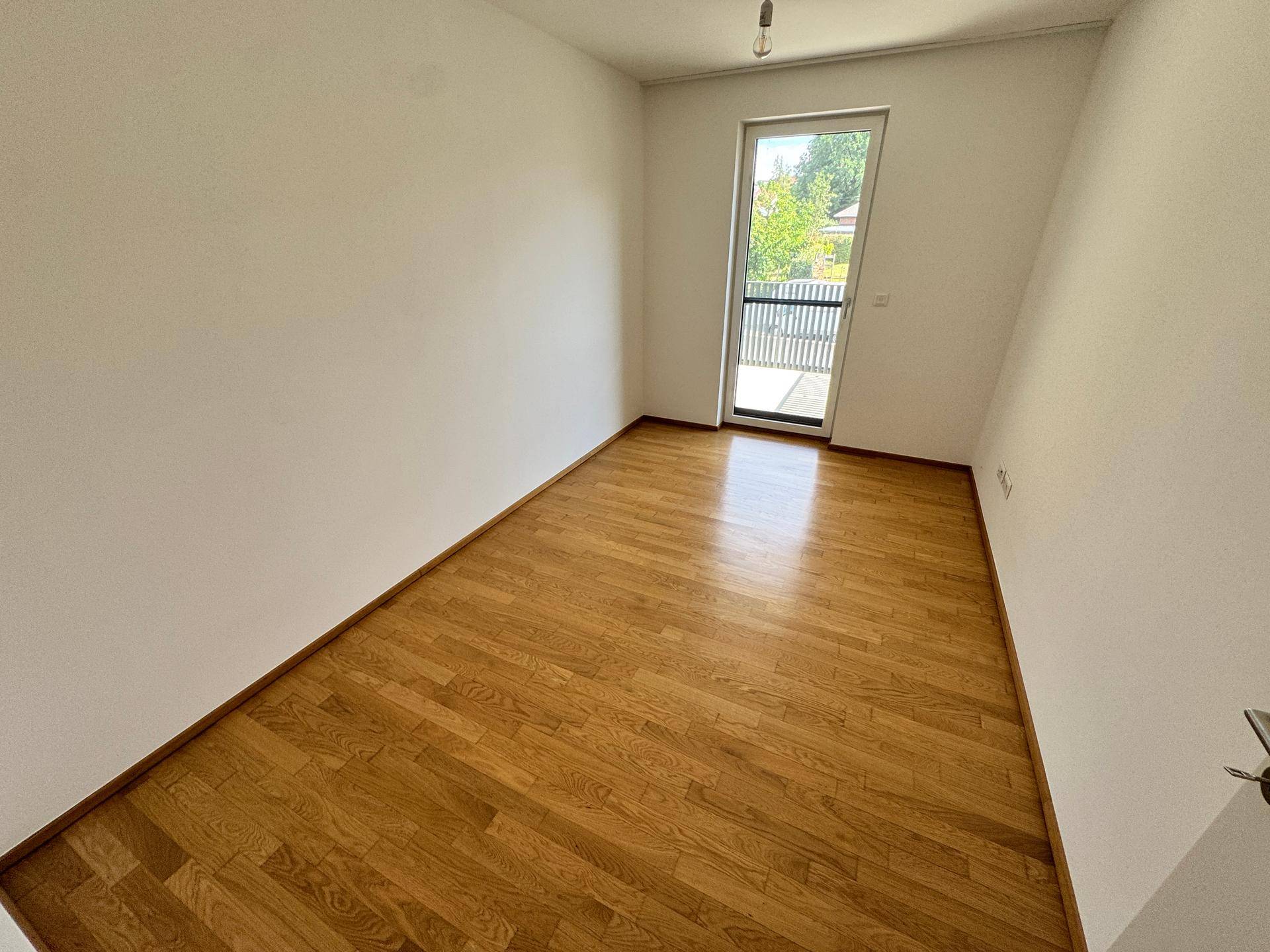 Helles Zimmer mit Holzboden und Zugang zu einem Balkon, ideal als Schlaf- oder Arbeitszimmer.