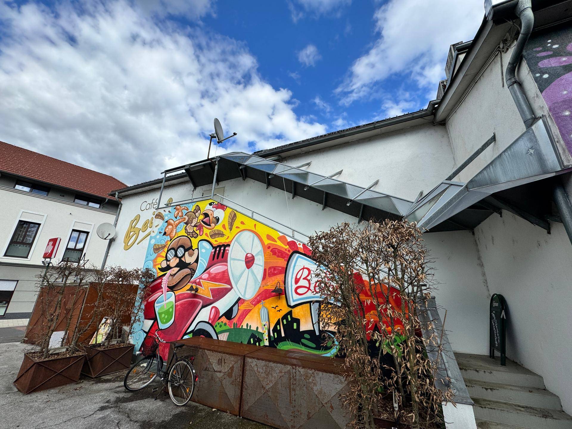 Gebäudeansicht mit lebhaftem Graffiti und einem schrägen Glasdach über dem Eingangsbereich.