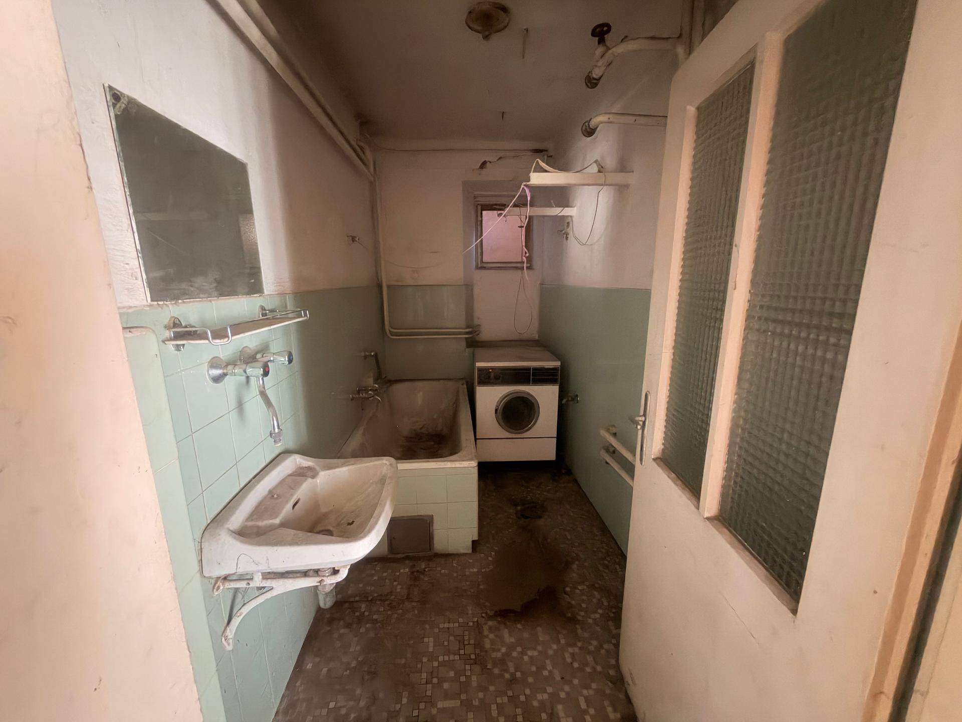 Altes Badezimmer mit Badewanne, Waschbecken und Waschmaschine, in schlechtem Zustand.
