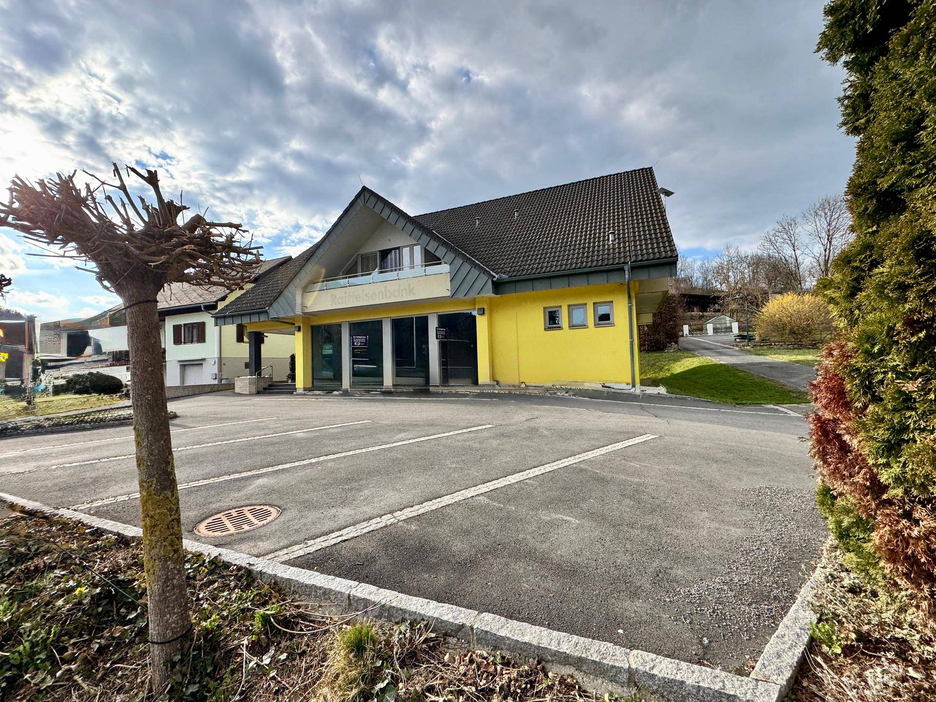 Ansicht des gelben Gebäudes mit Parkplatz und umliegender grüner Landschaft.